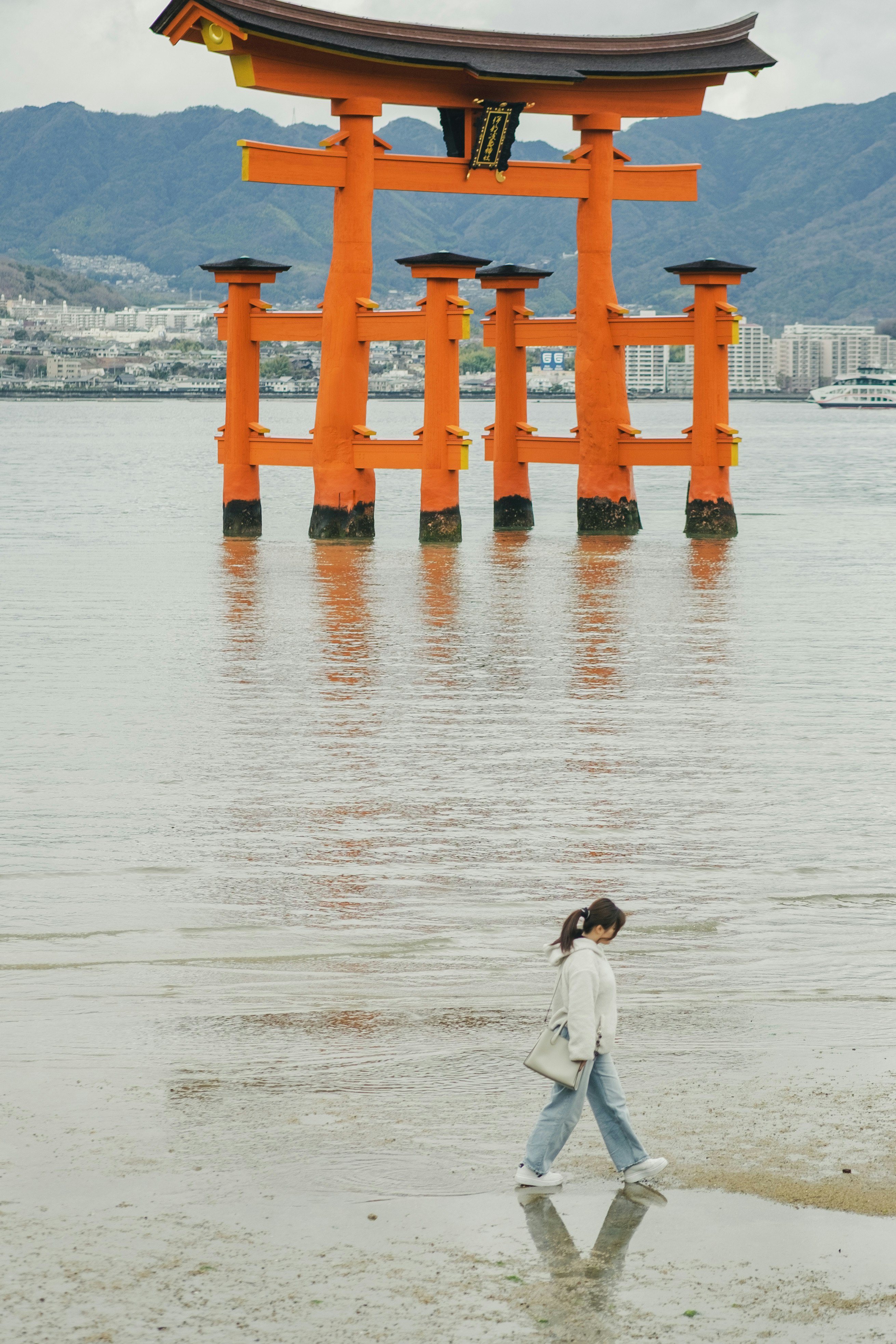 Orange torii gate standing in the water with a woman walking in front