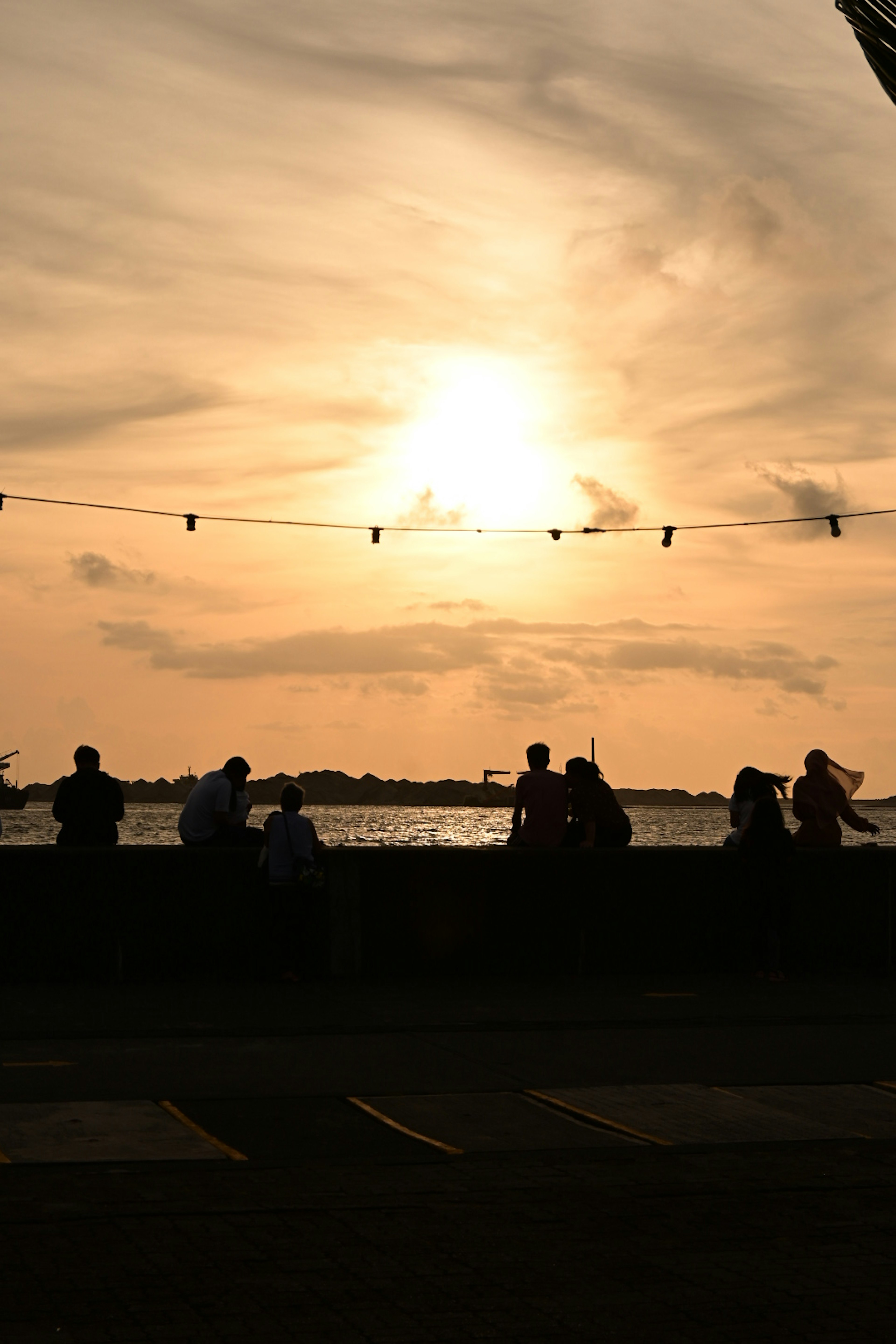 Silhouettes of people sitting along a waterfront at sunset