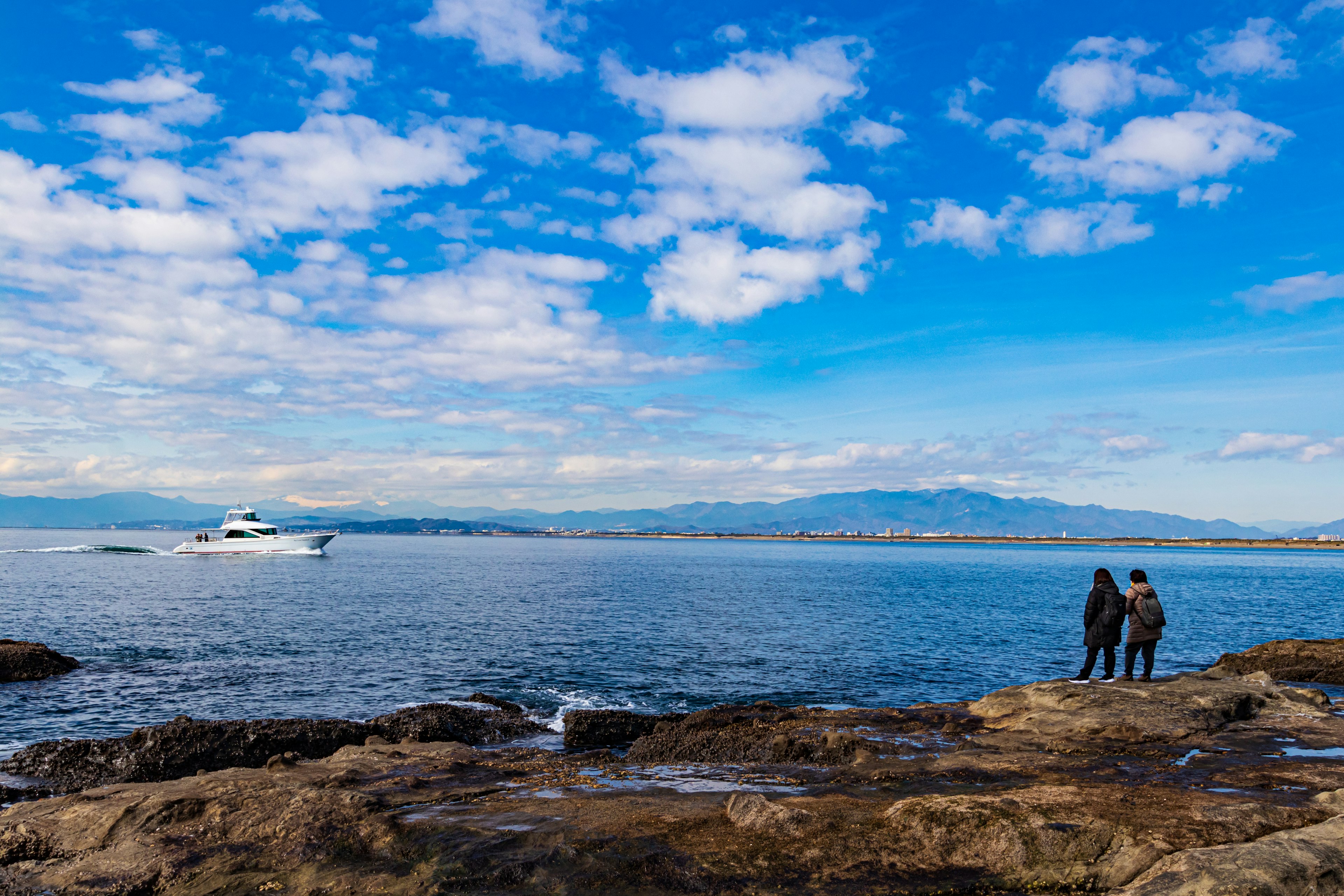 Paar steht auf Felsen am Meer unter einem blauen Himmel mit Wolken