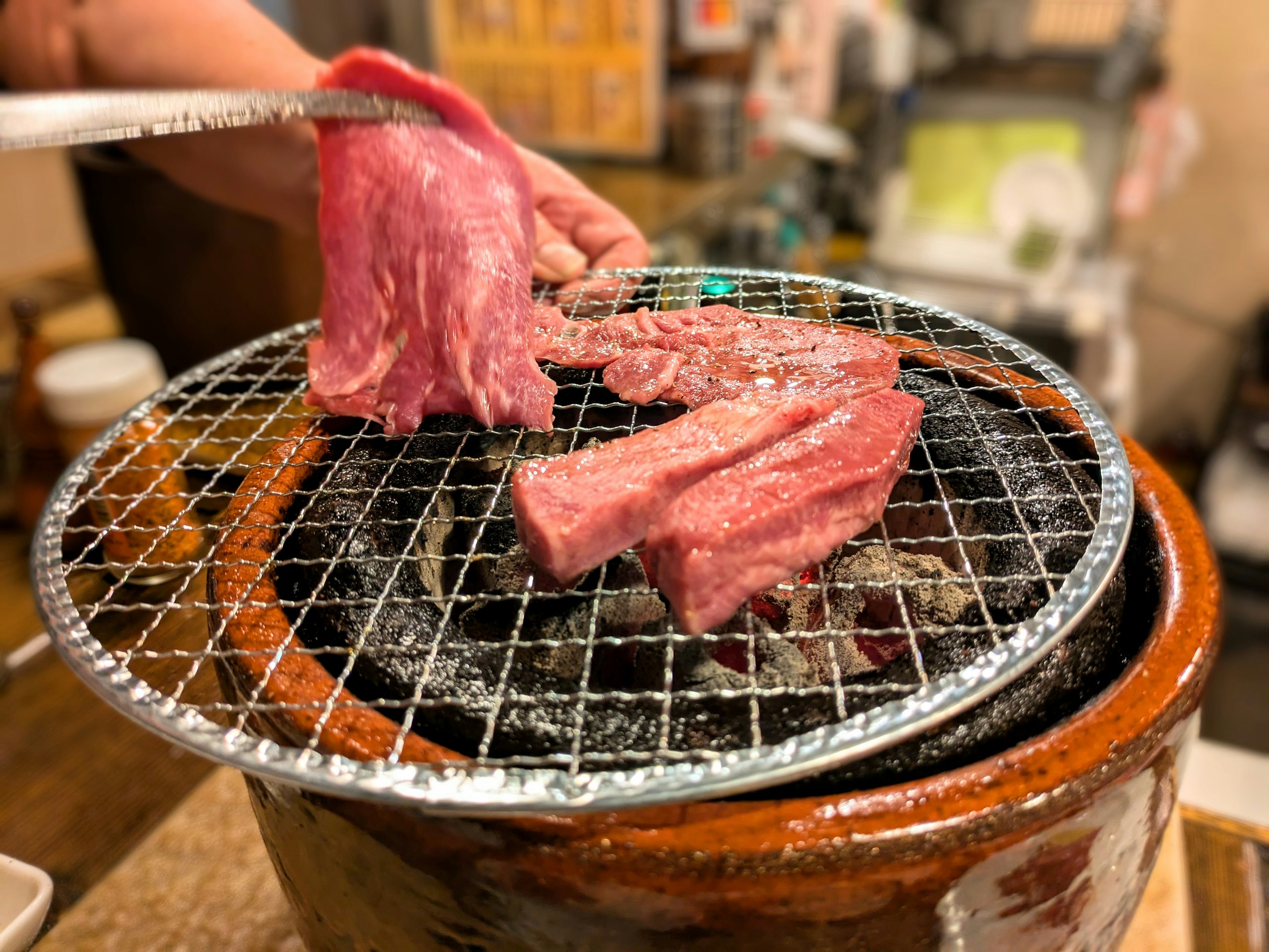 焼き肉の網の上で肉を焼いている手