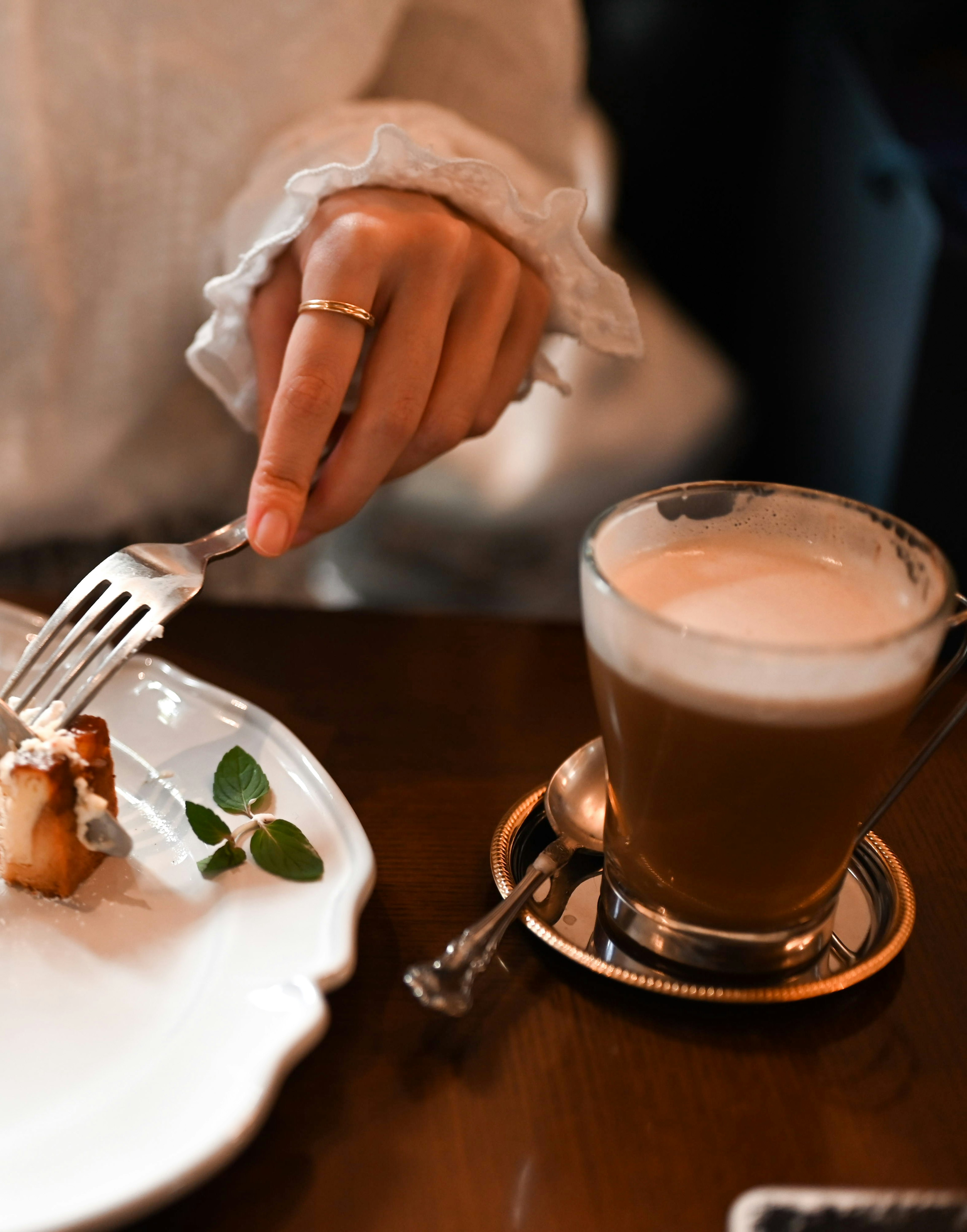 Eine Hand hält eine Gabel, bereit, ein Gericht auf einem Teller zu essen, mit einer Kaffeetasse daneben