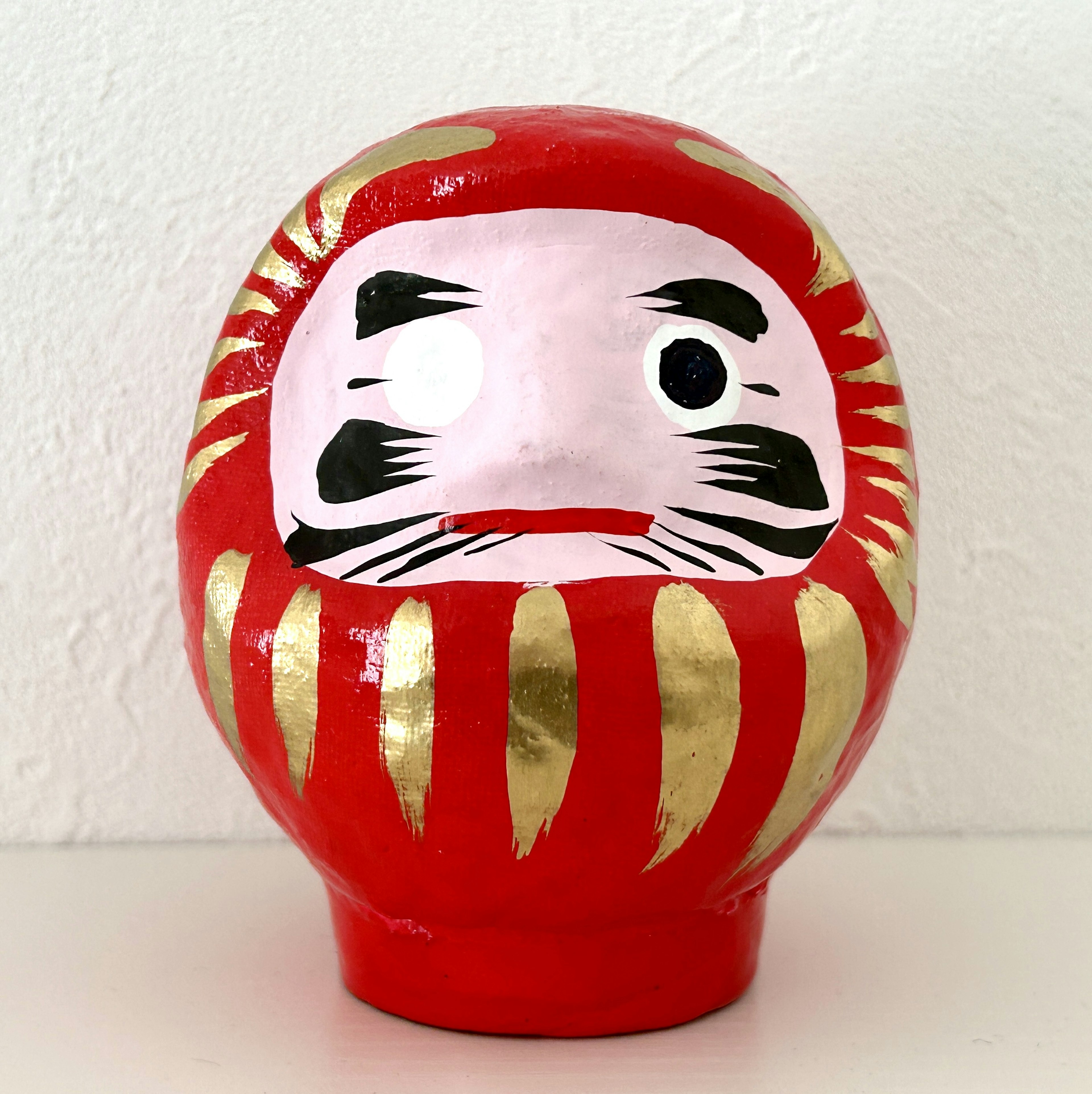 Red Daruma doll with gold stripes and facial features