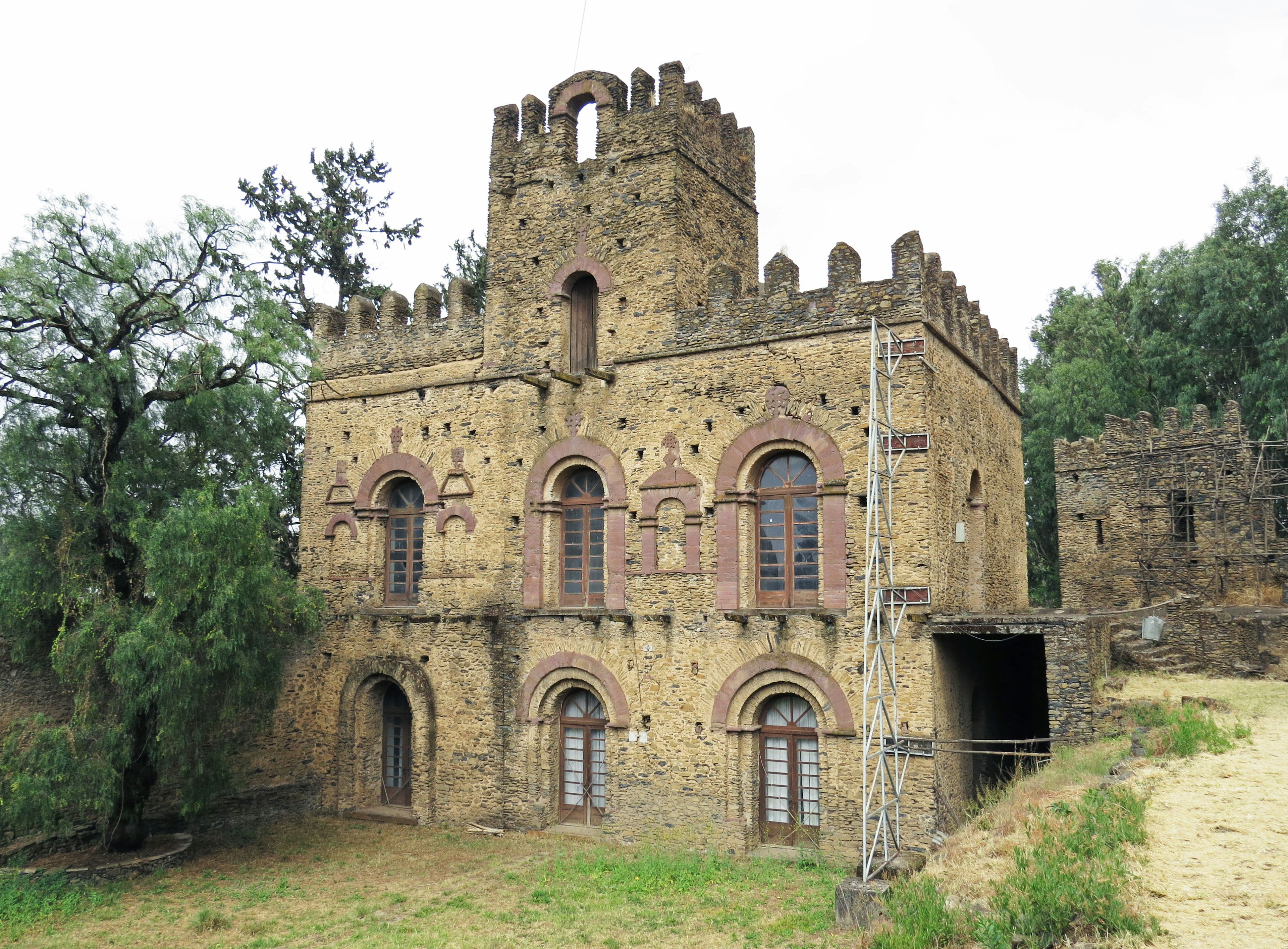 Vecchio edificio simile a un castello circondato da vegetazione con muri in pietra e torri