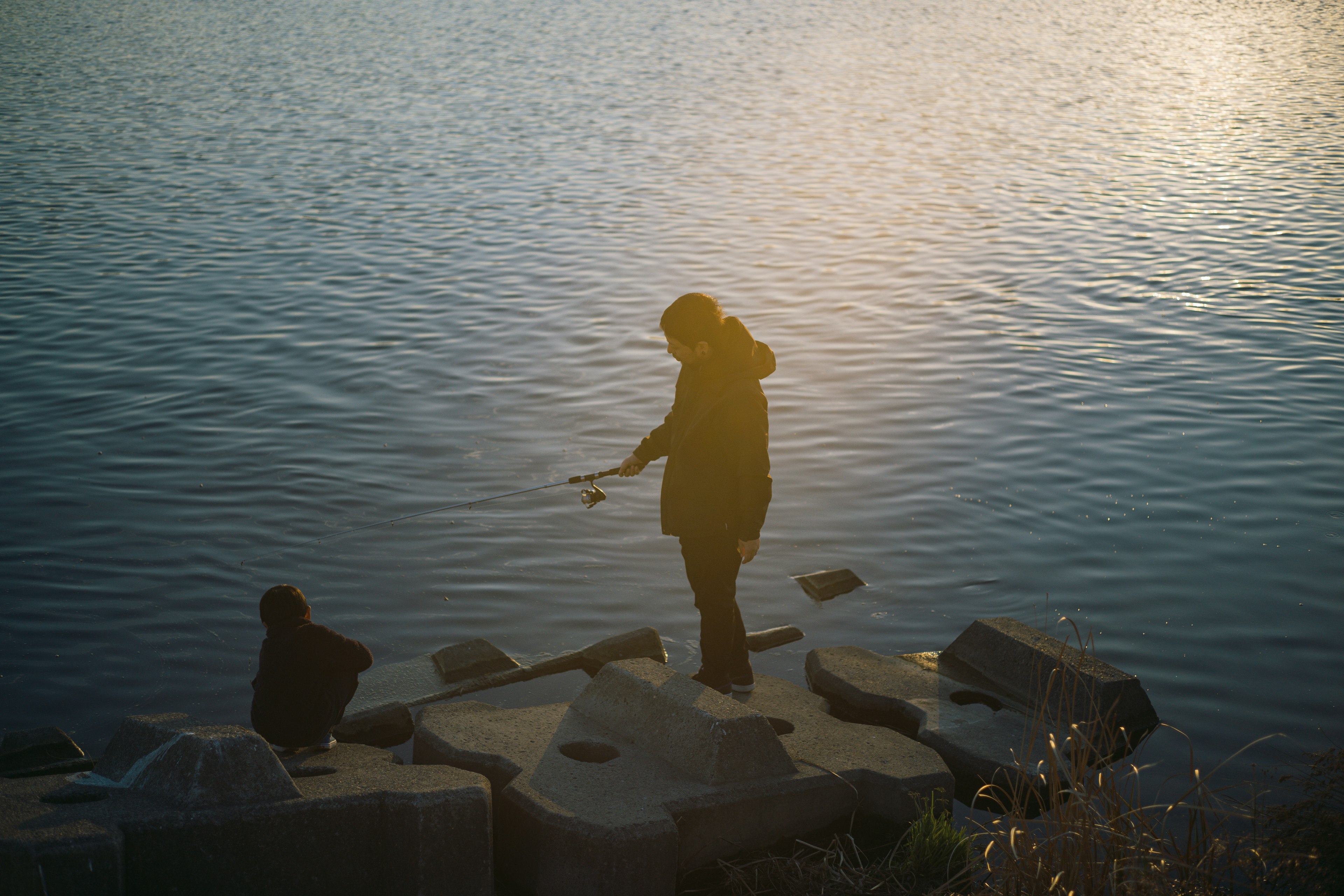 Silhouette von zwei Personen, die am Wasser fischen