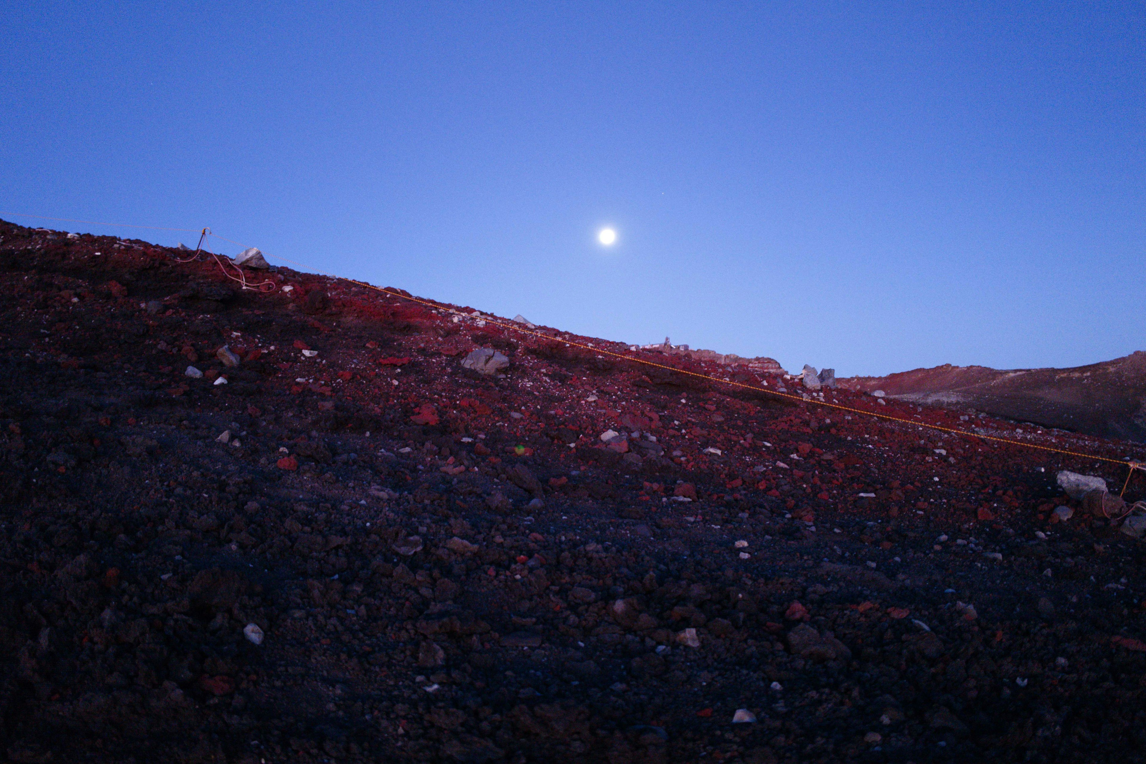 Luna brillante en un cielo azul sobre una colina de tierra roja