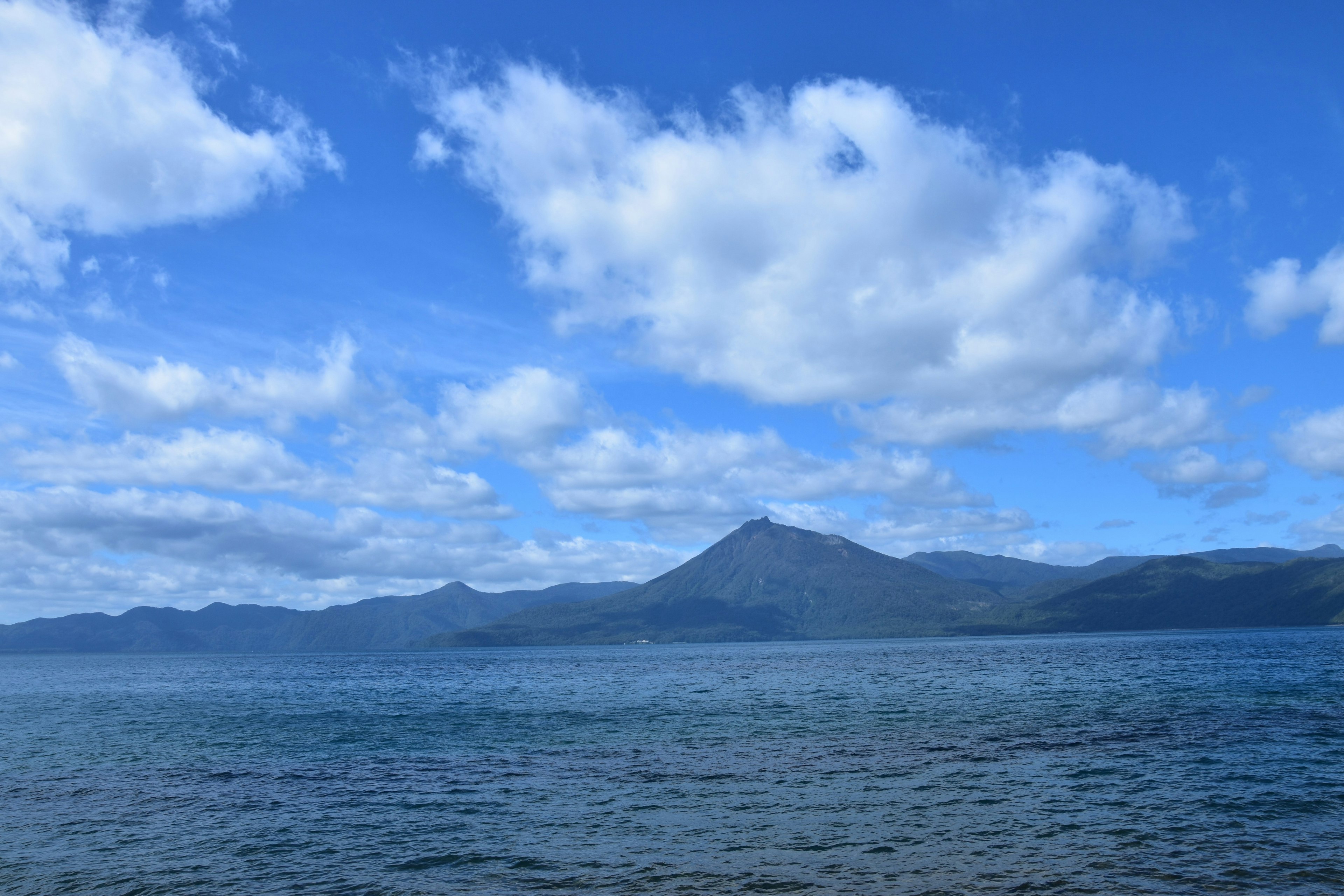 青い空と白い雲の下に広がる静かな湖と山々の風景