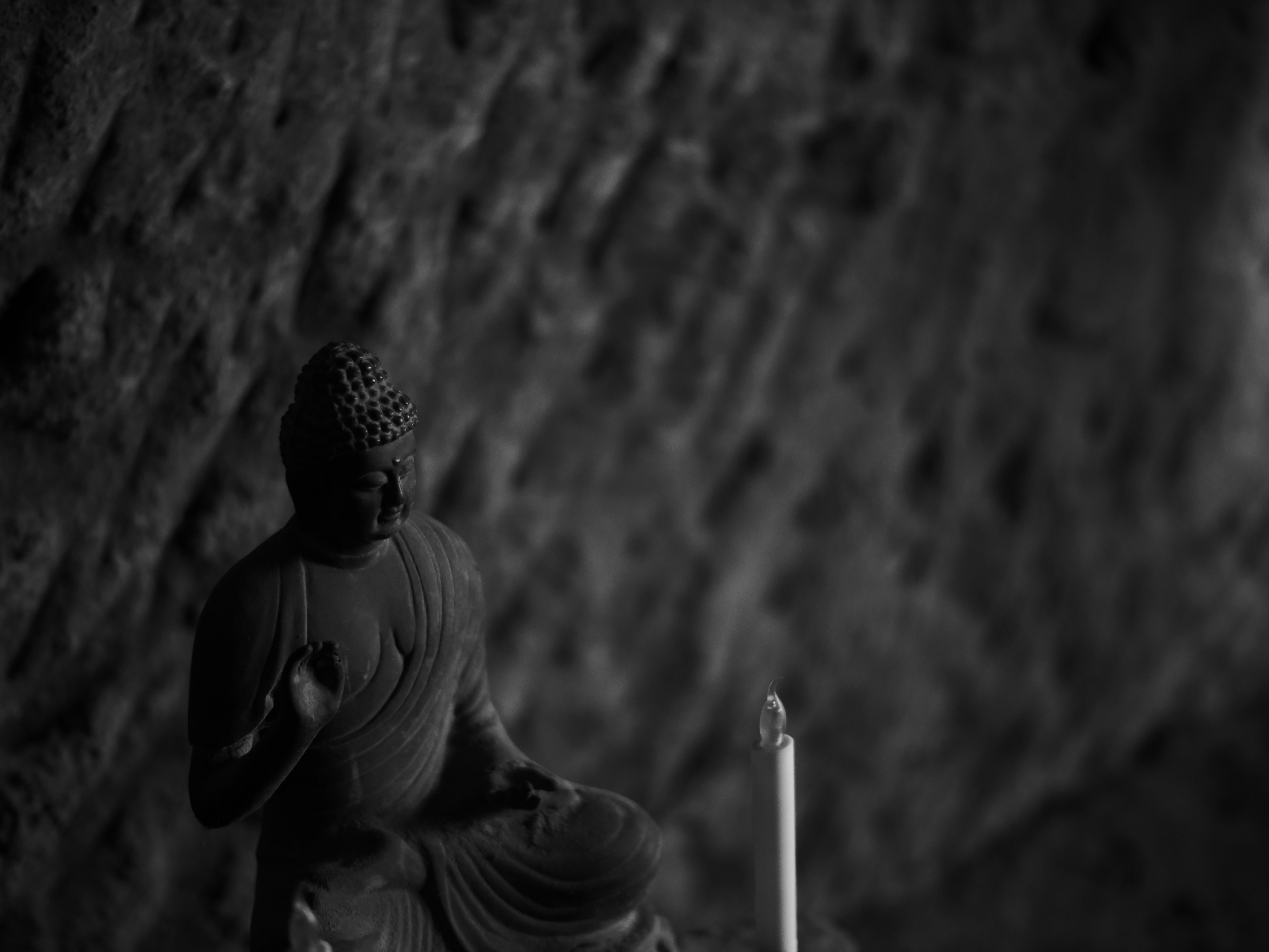 Black and white statue of Buddha seated against a rocky background with a candle nearby