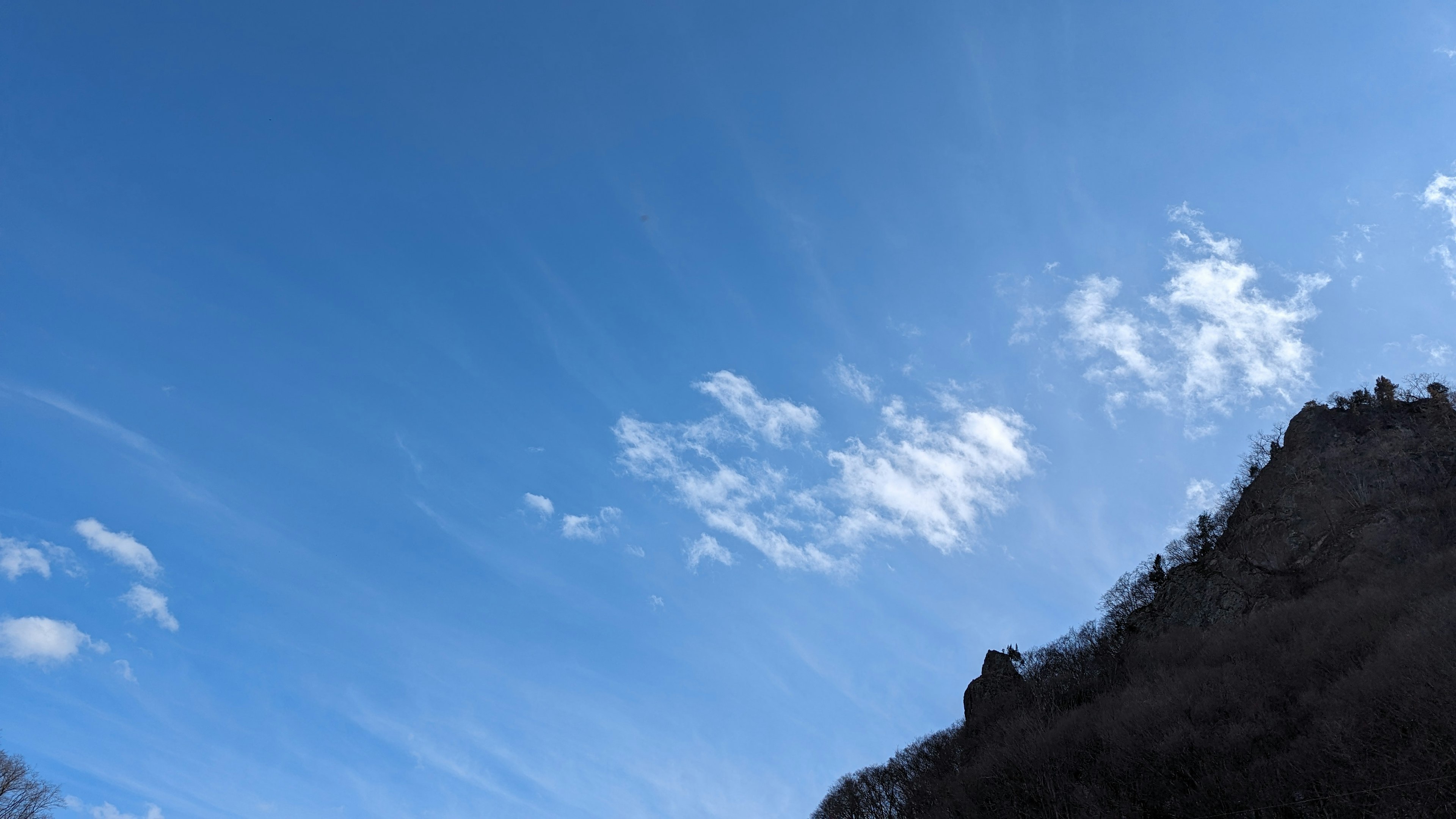 A view of a blue sky with white clouds and a mountain silhouette