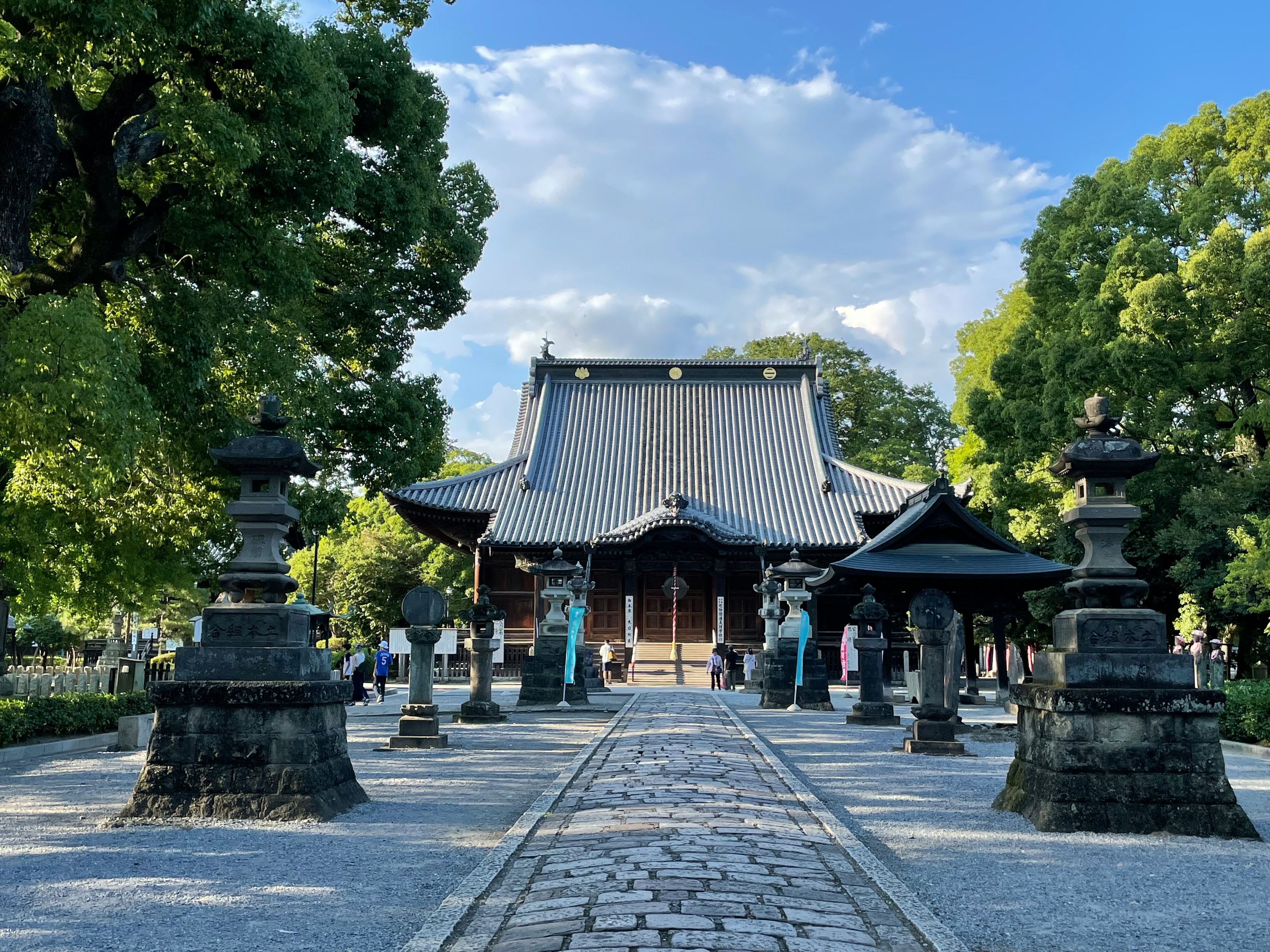 美しい神社の入り口に続く石の道、両側には石灯篭と緑豊かな木々が並んでいる