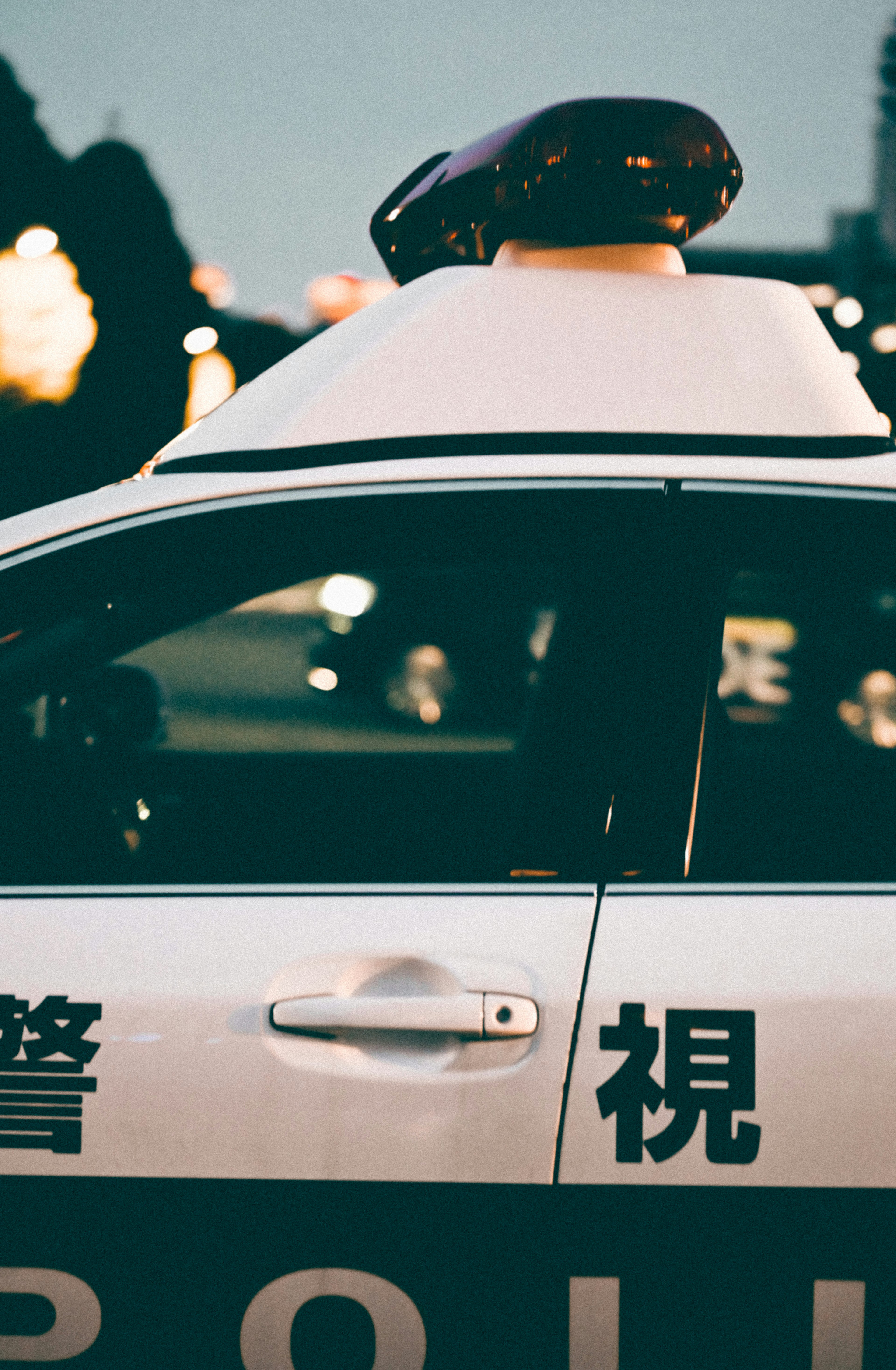 Image of a police vehicle with a red and blue light on the roof featuring Japanese characters on the side