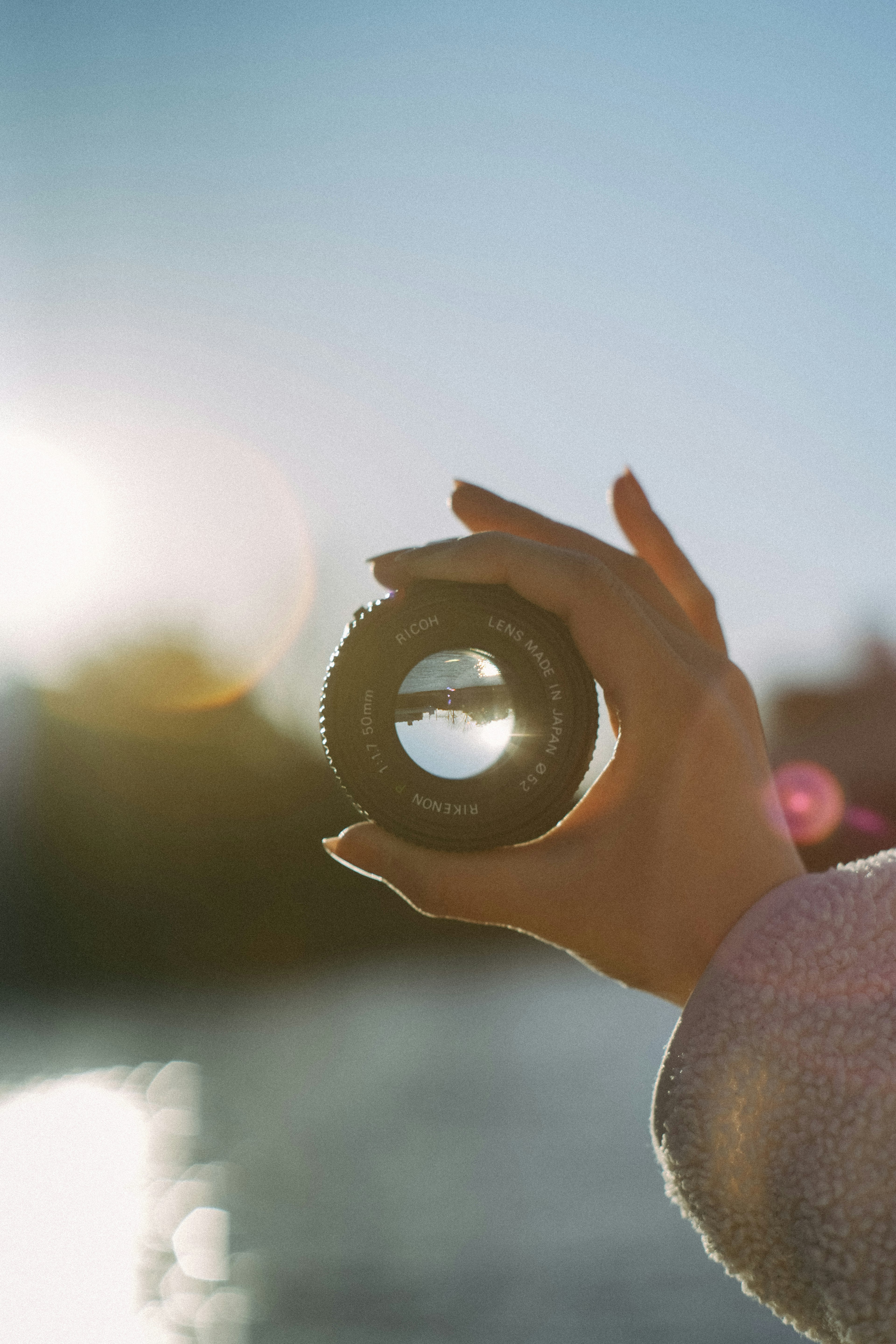 Silhouette einer Hand, die ein Objektiv vor einem verschwommenen, sonnigen Hintergrund hält