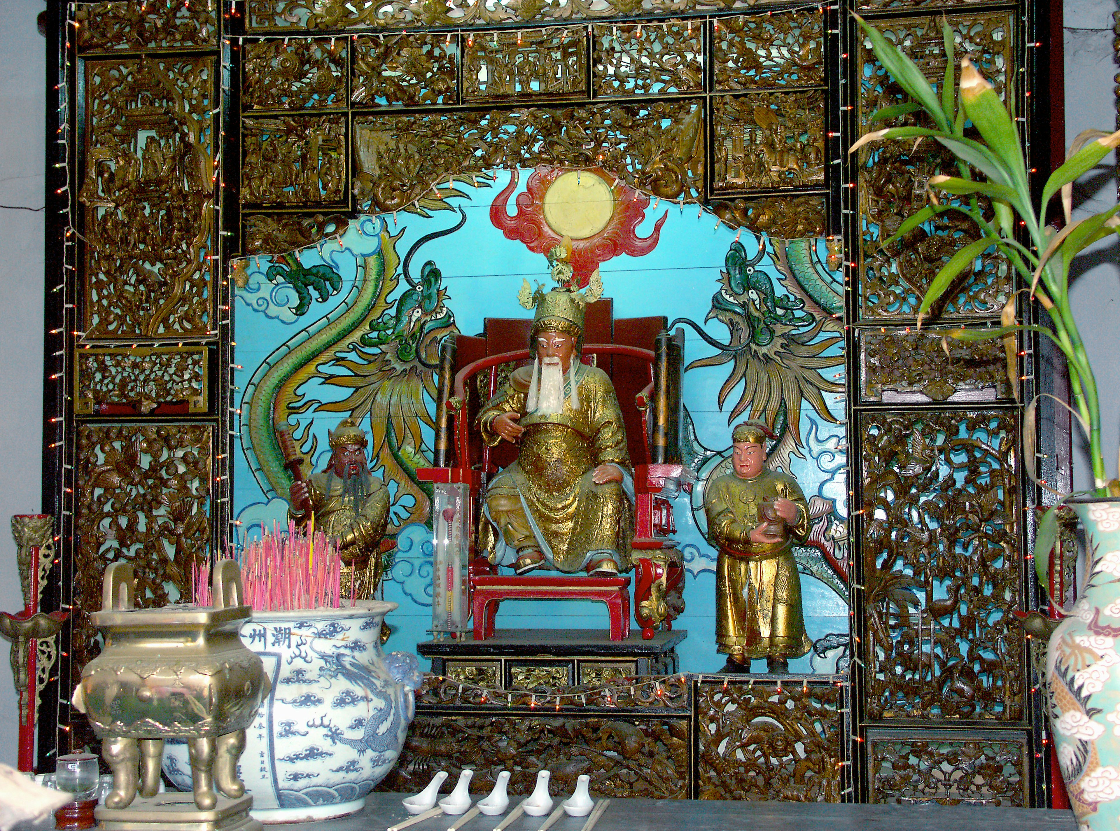 Image of a golden seated deity surrounded by intricate decorations and incense