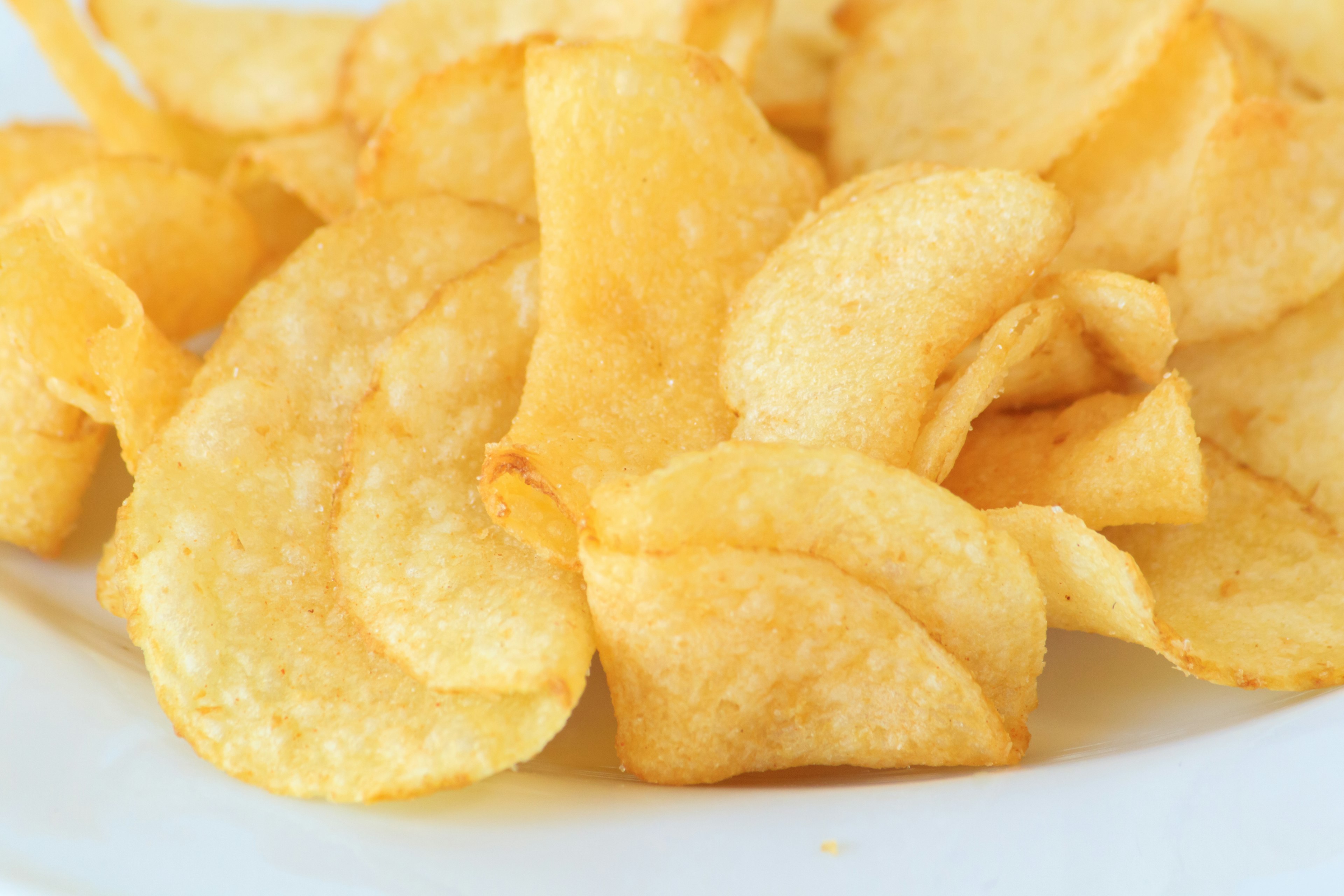 Dünn frittierte Kartoffelchips auf einem weißen Teller angeordnet