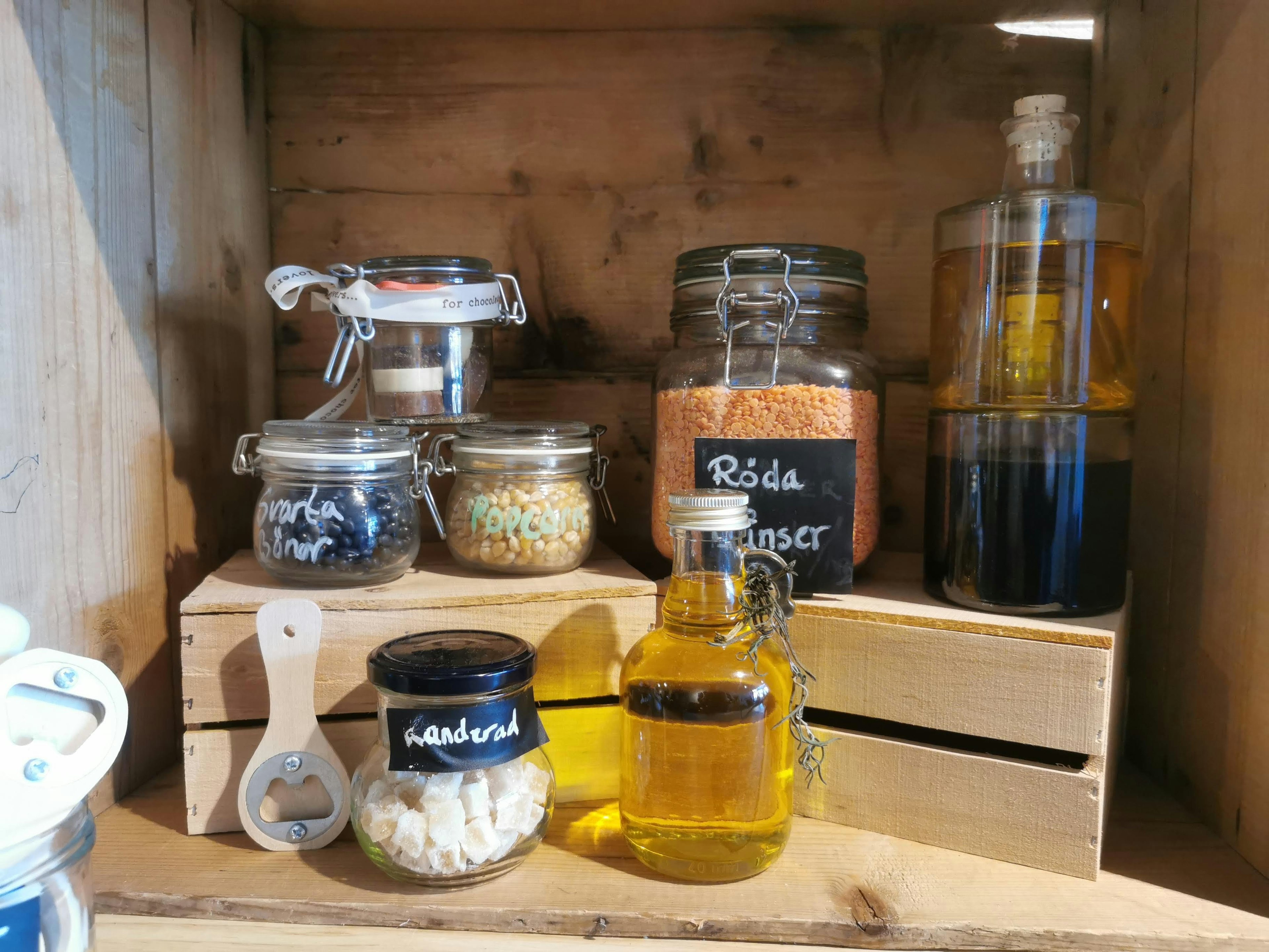 Glass jars and oil bottles arranged on a wooden shelf containing various spices and ingredients