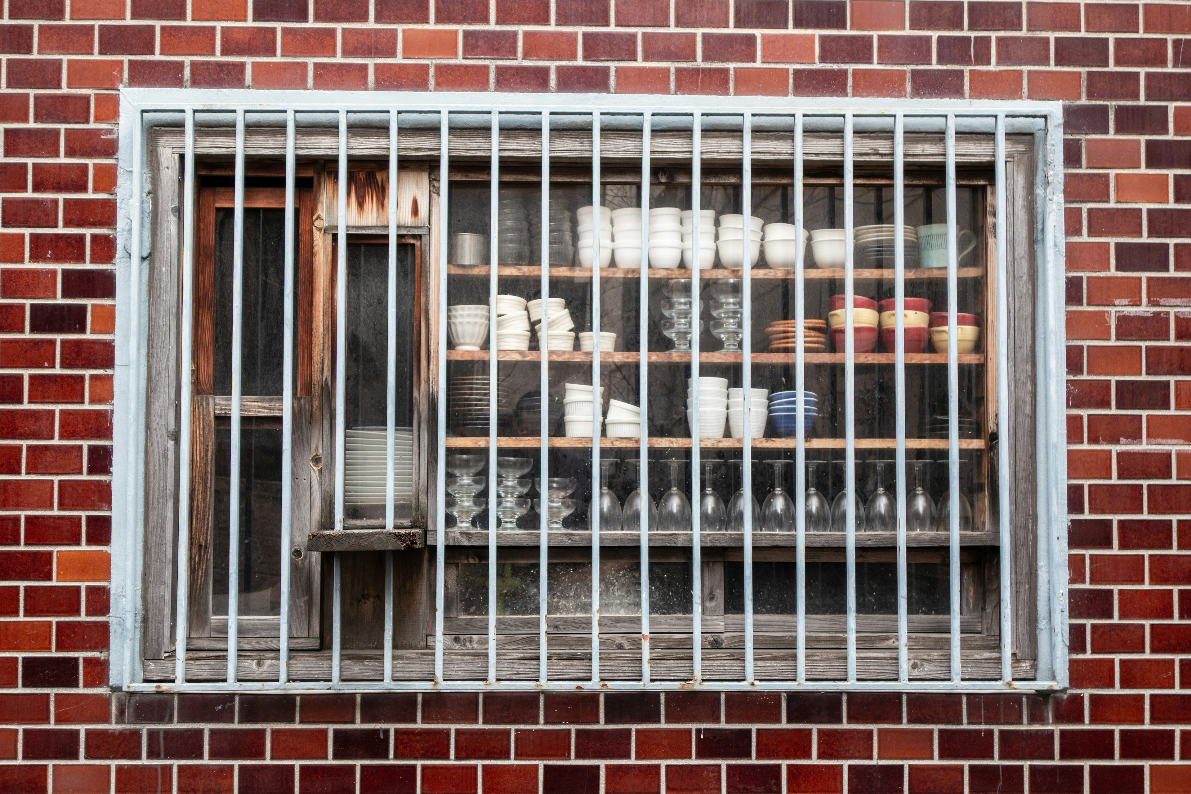 Window with bars showcasing pottery and glassware against a red brick wall