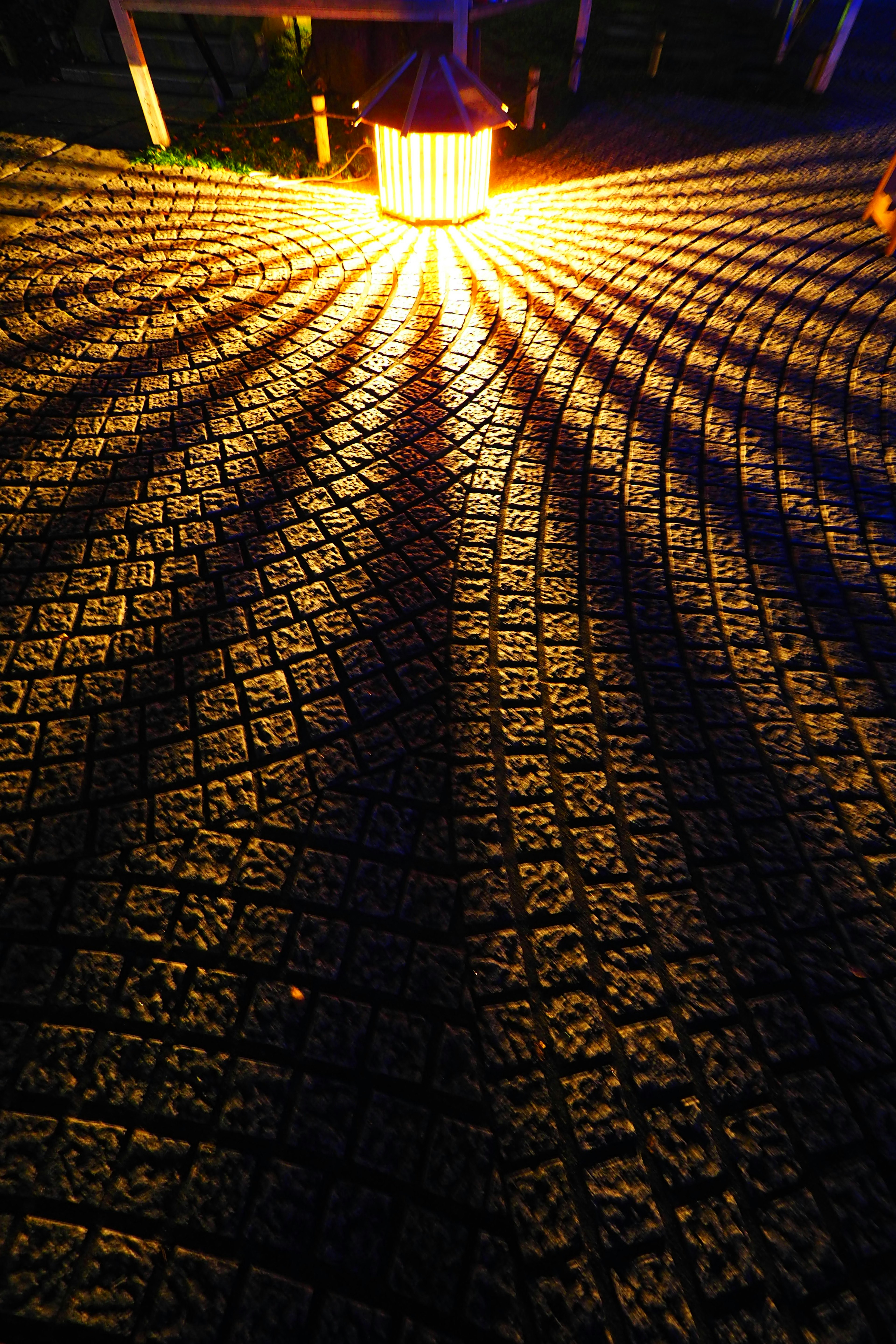 Bright lantern light casting dramatic shadows on textured pavement