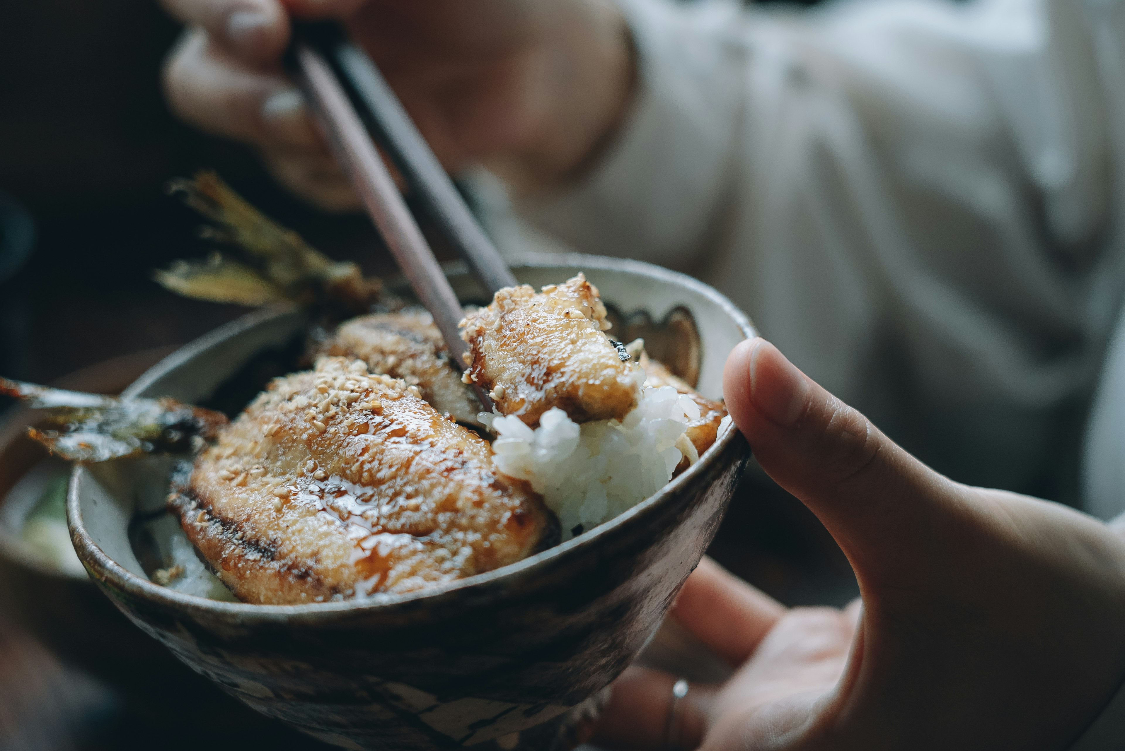 A stylish bowl held in hand containing rice and grilled fish