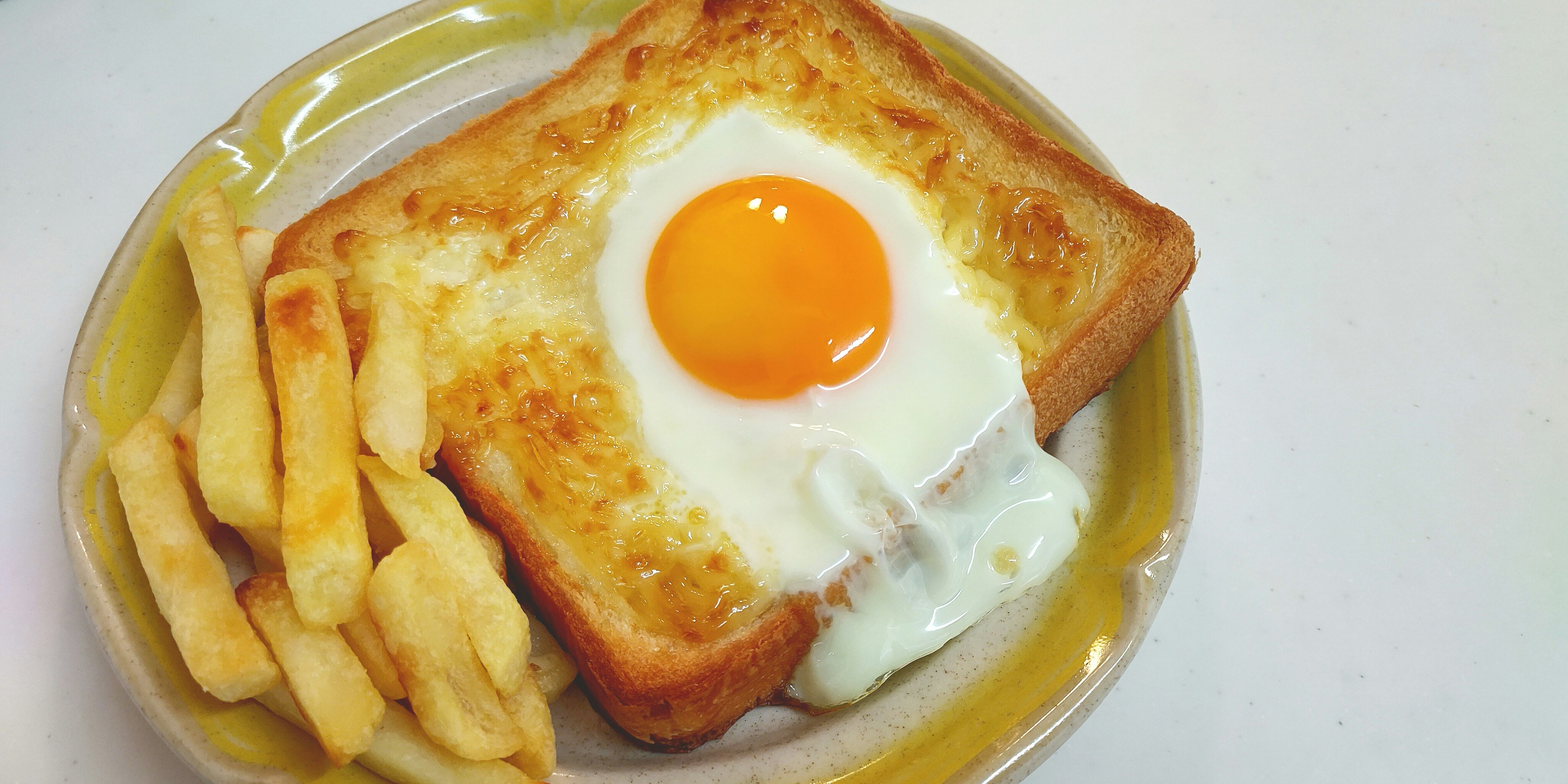 Piatto per colazione con toast guarnito da un uovo fritto e patatine fritte