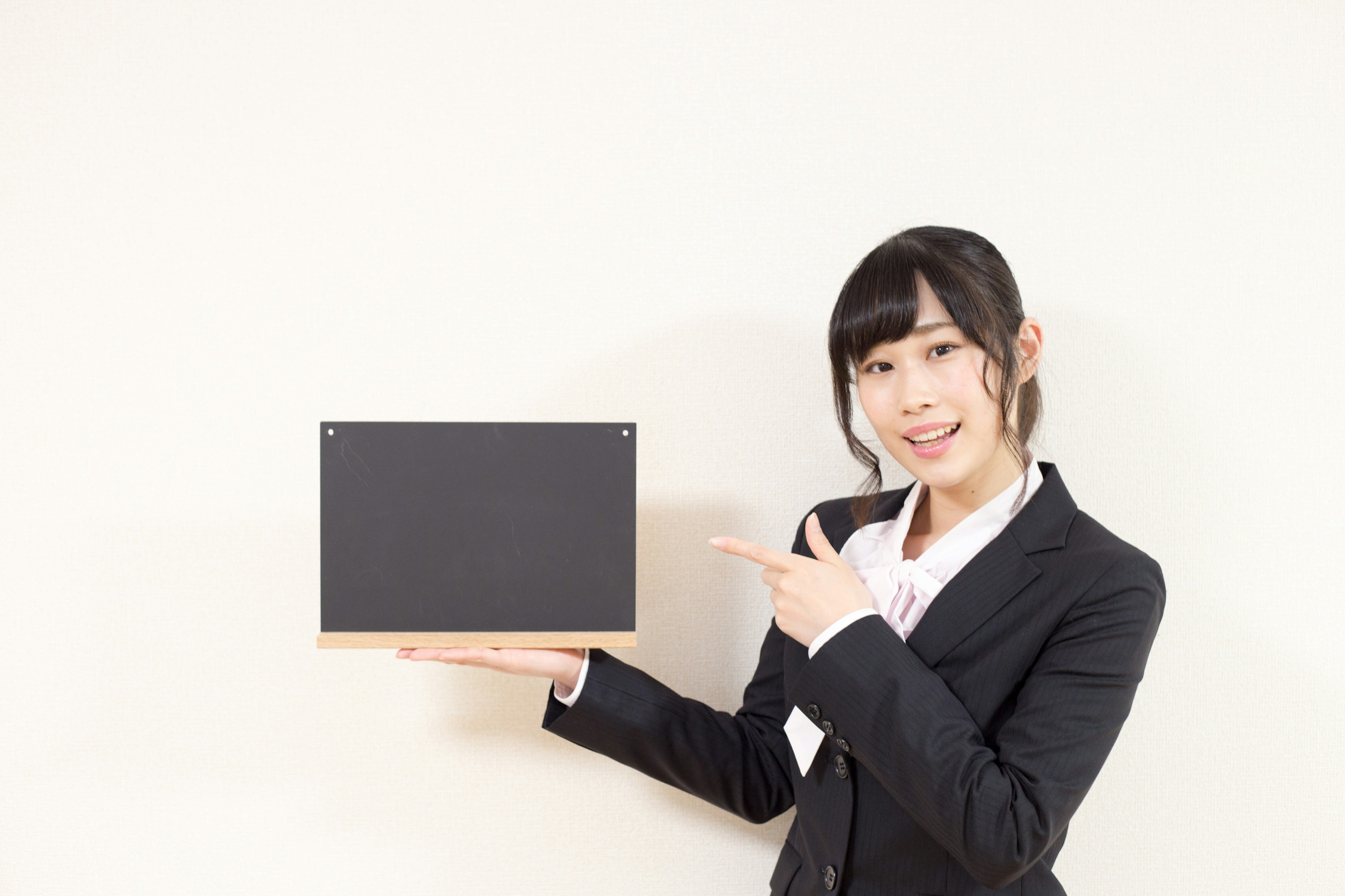 A woman in a business suit smiling while holding a black board