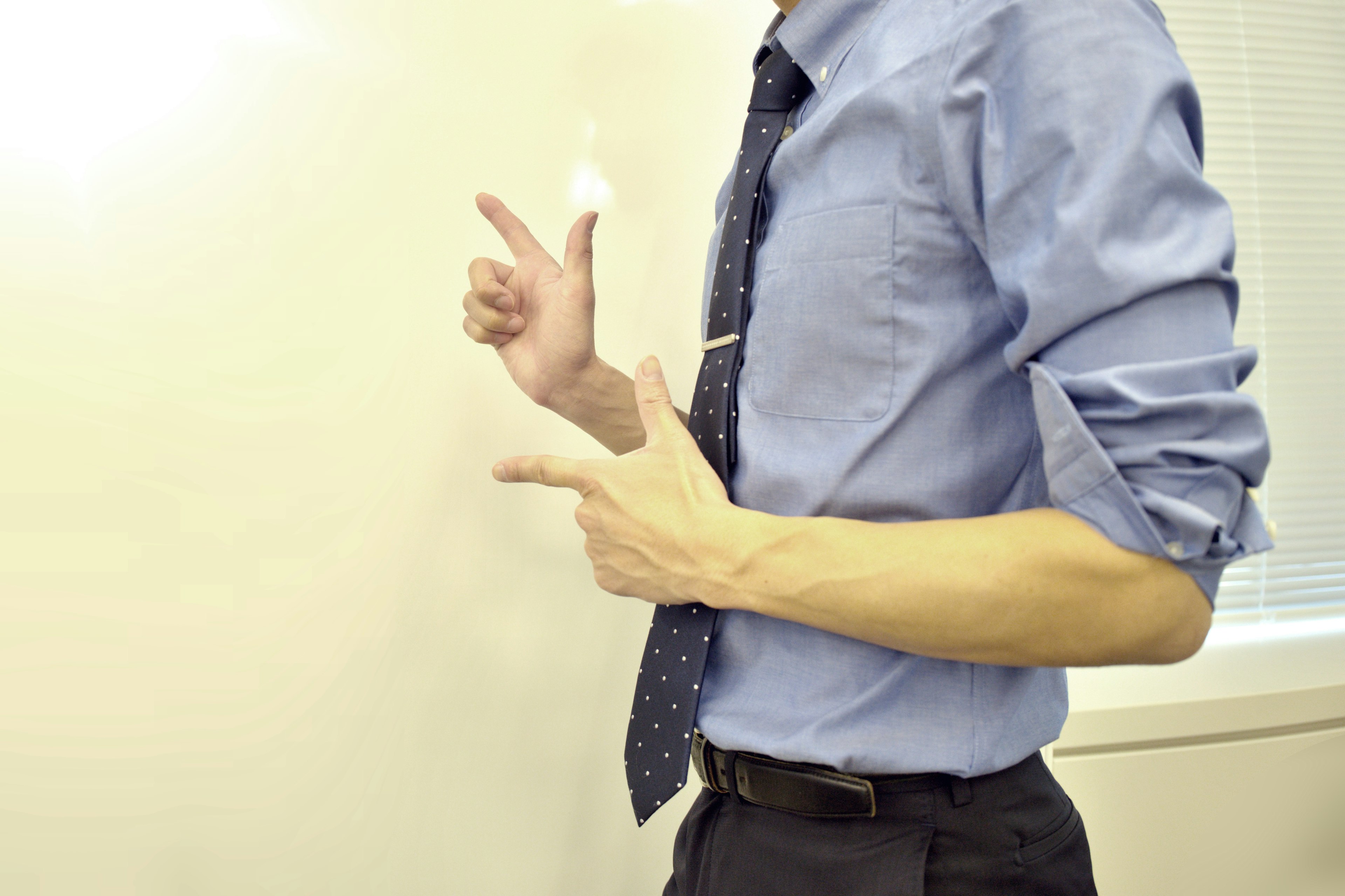 Un uomo in camicia blu e cravatta che punta verso un muro