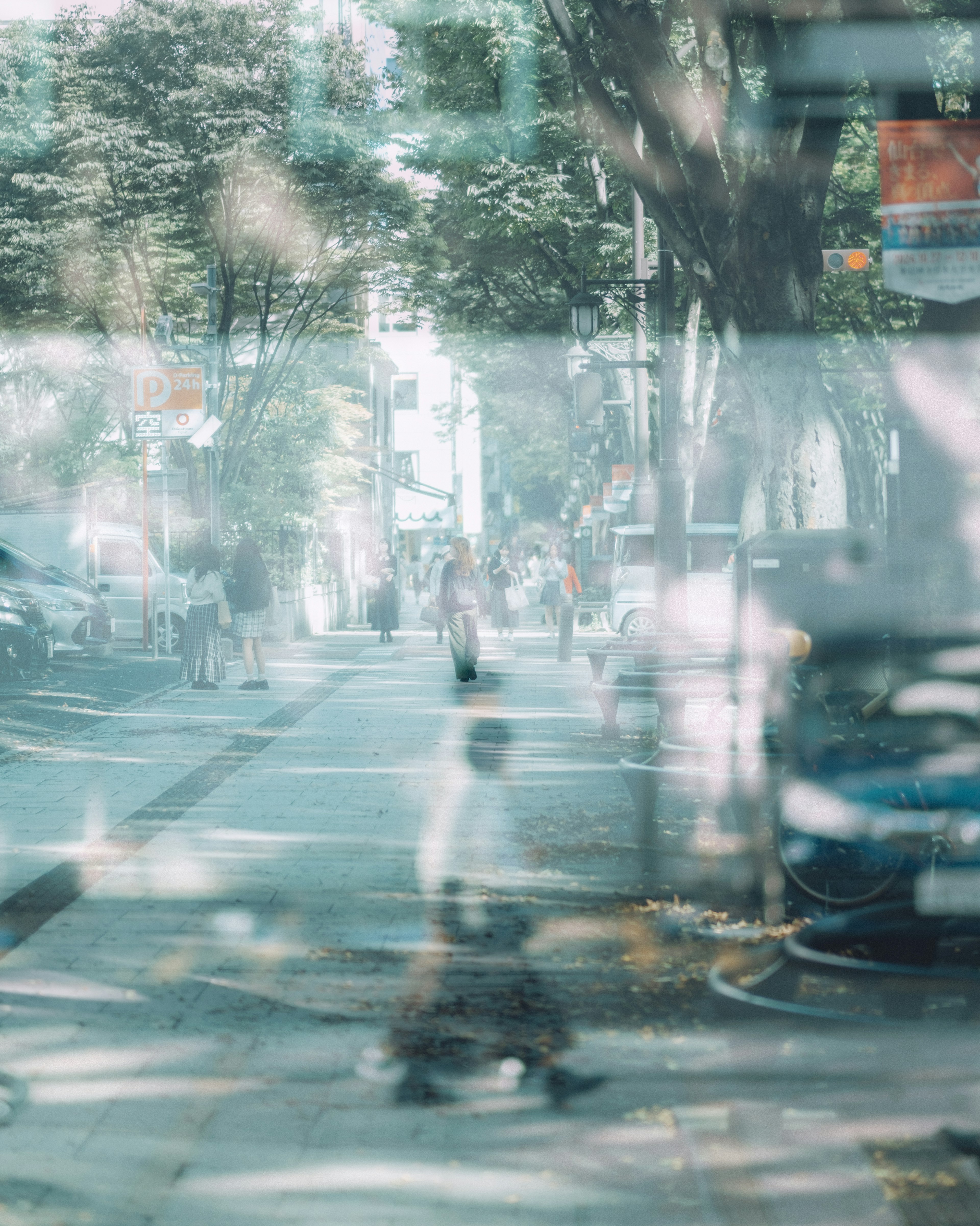 Blurred street scene with people walking trees and cars visible