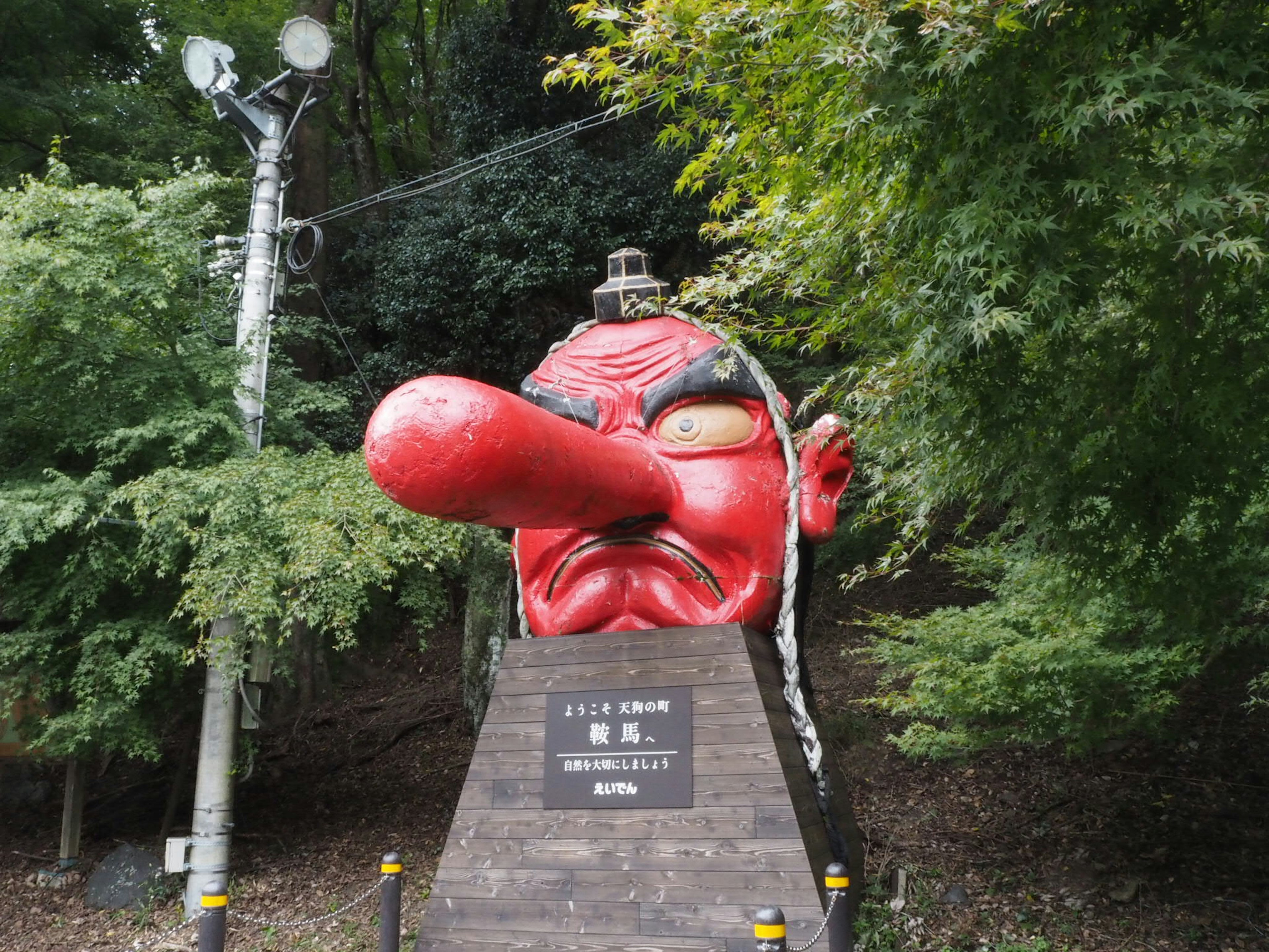 Giant sculpture with a red face and long nose surrounded by green trees