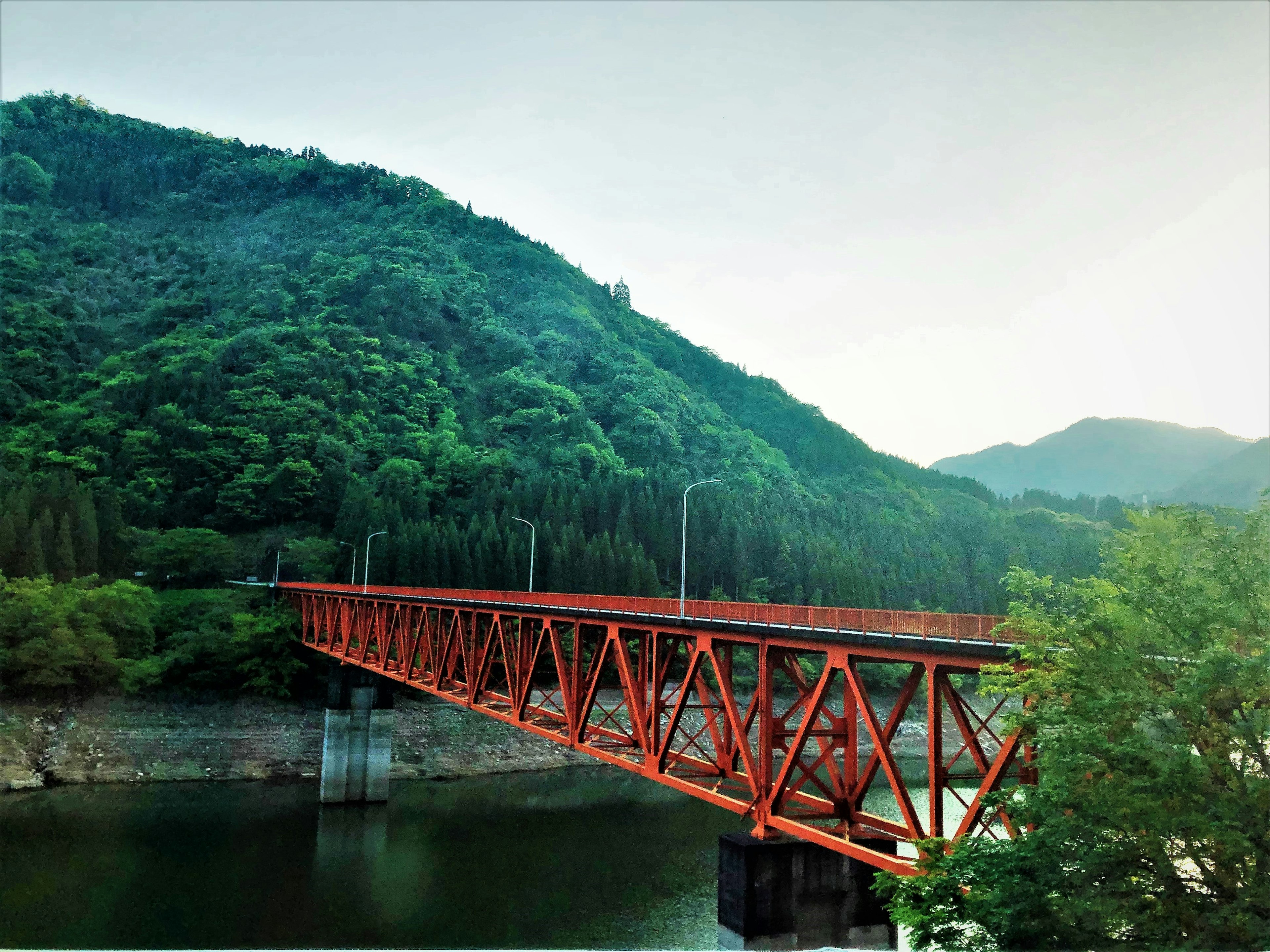 Red steel bridge set against lush green mountains