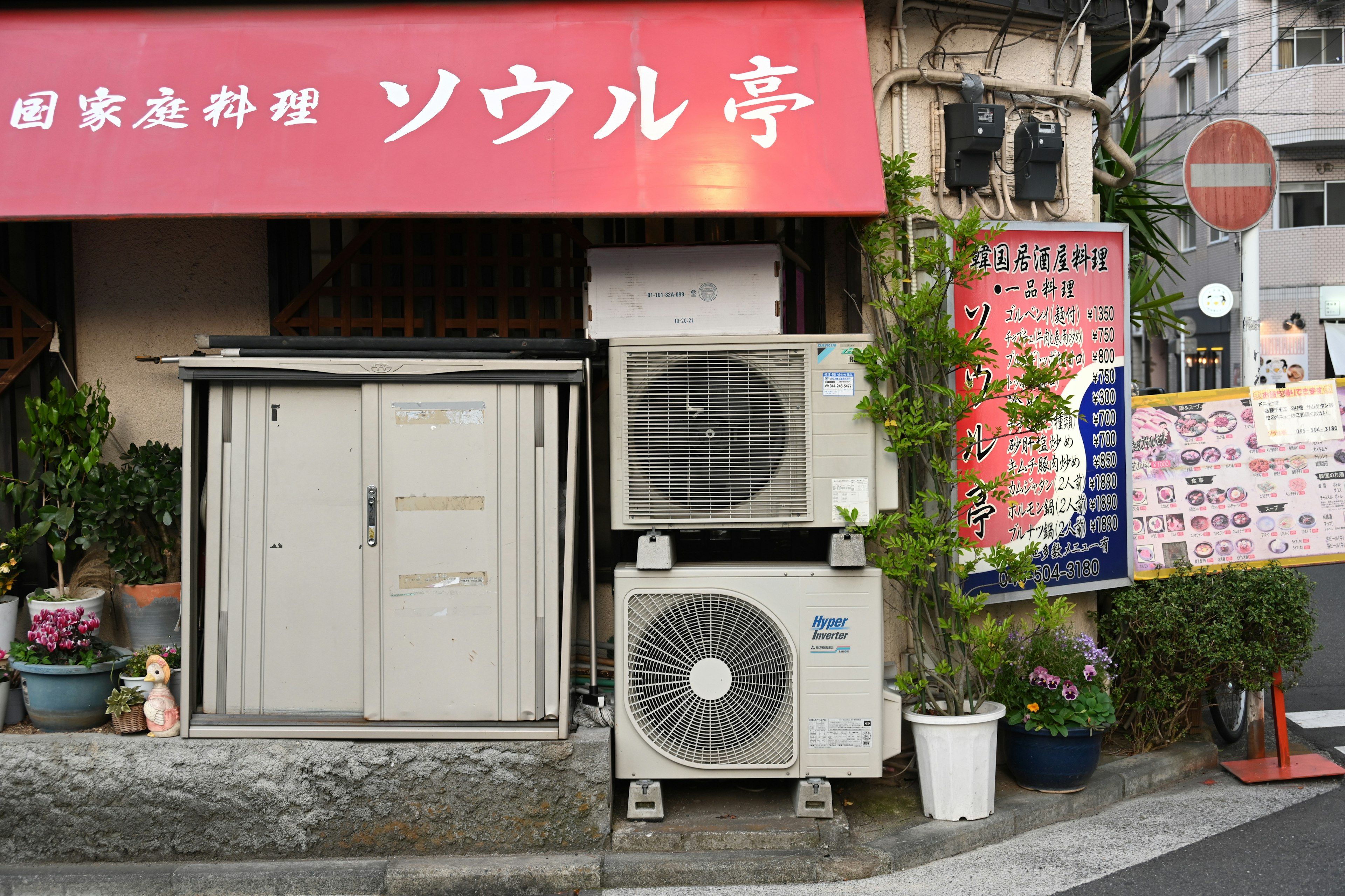 Unidades de aire acondicionado al lado del letrero rojo de Seoul Tei con plantas alrededor