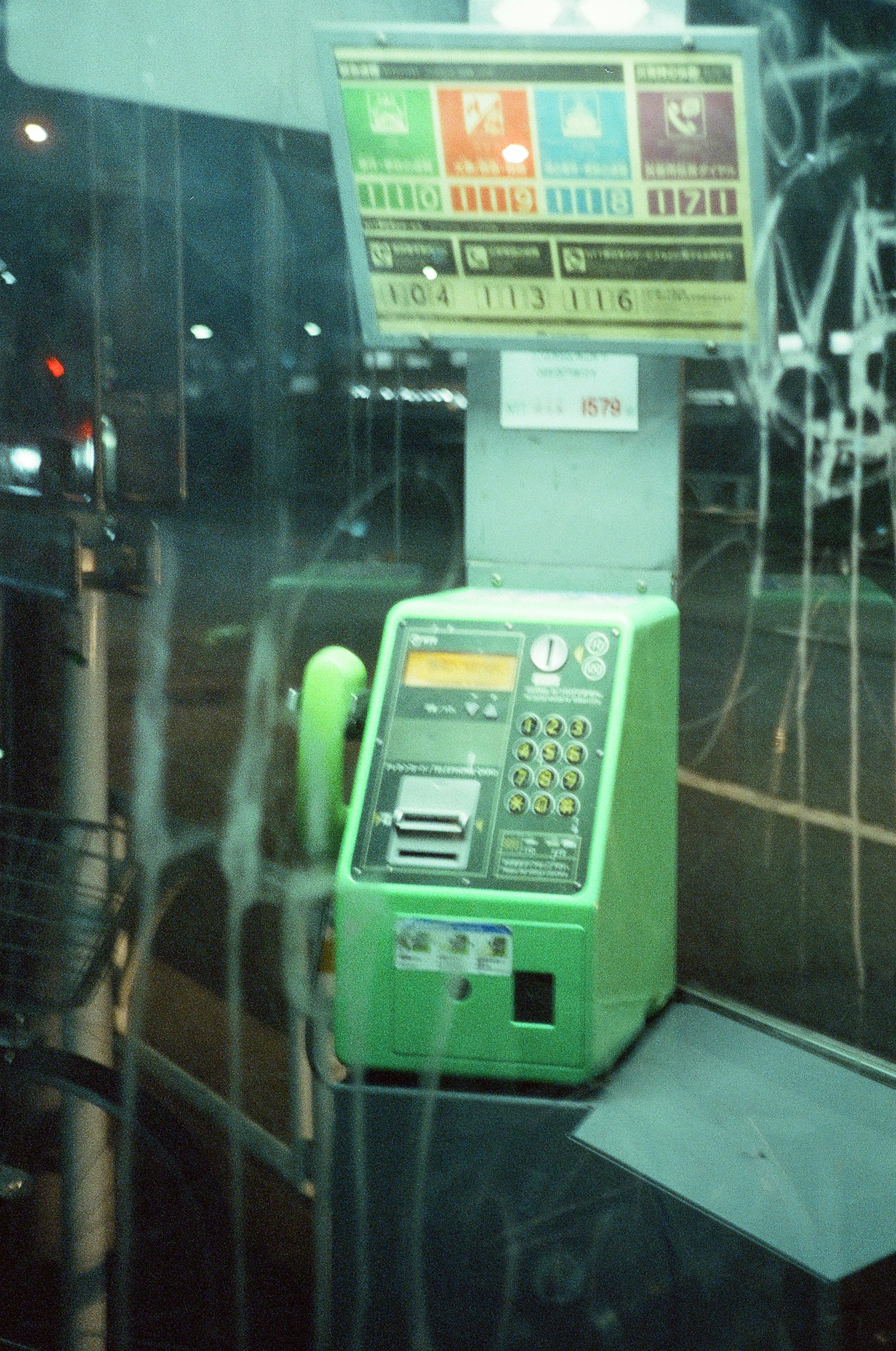 Old green payphone in a nighttime urban setting with visible buttons and display