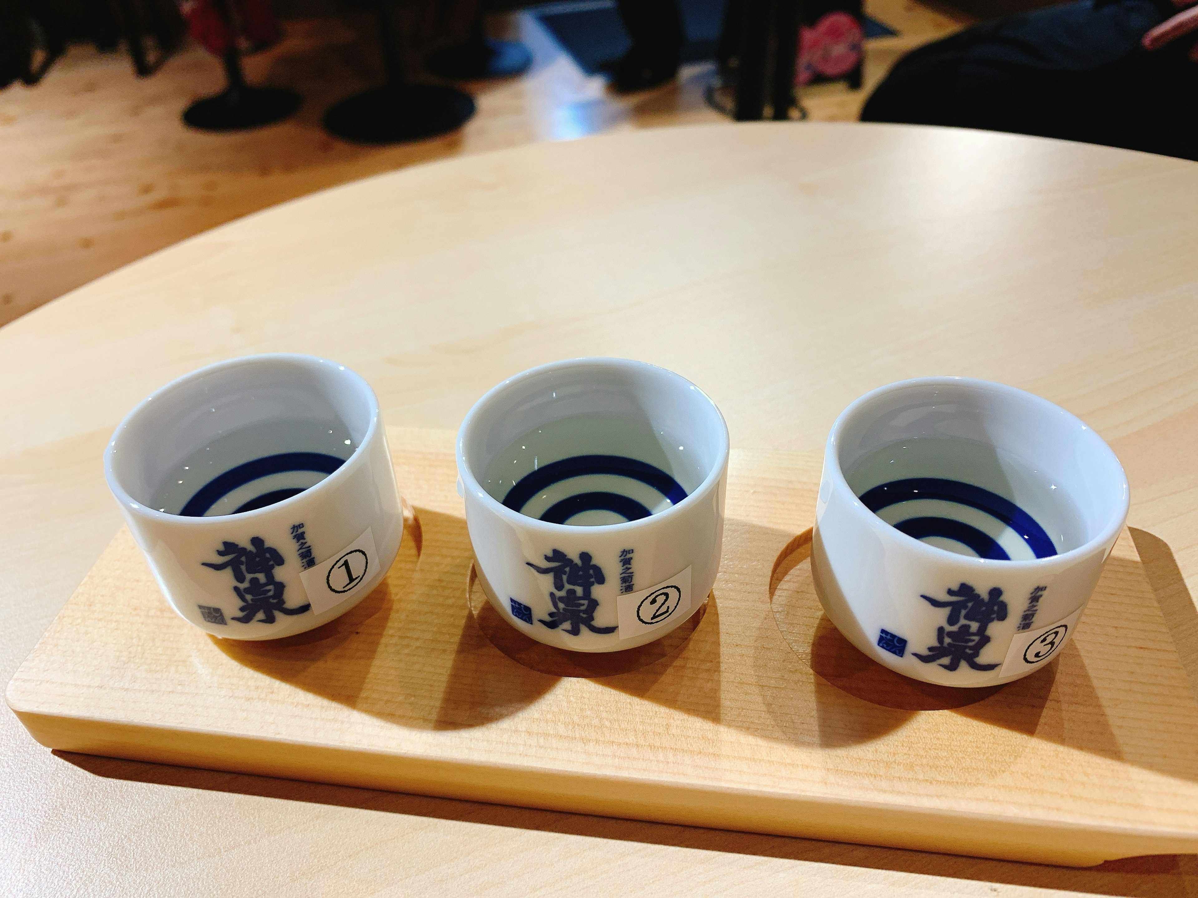 Three white sake cups arranged on a wooden tray