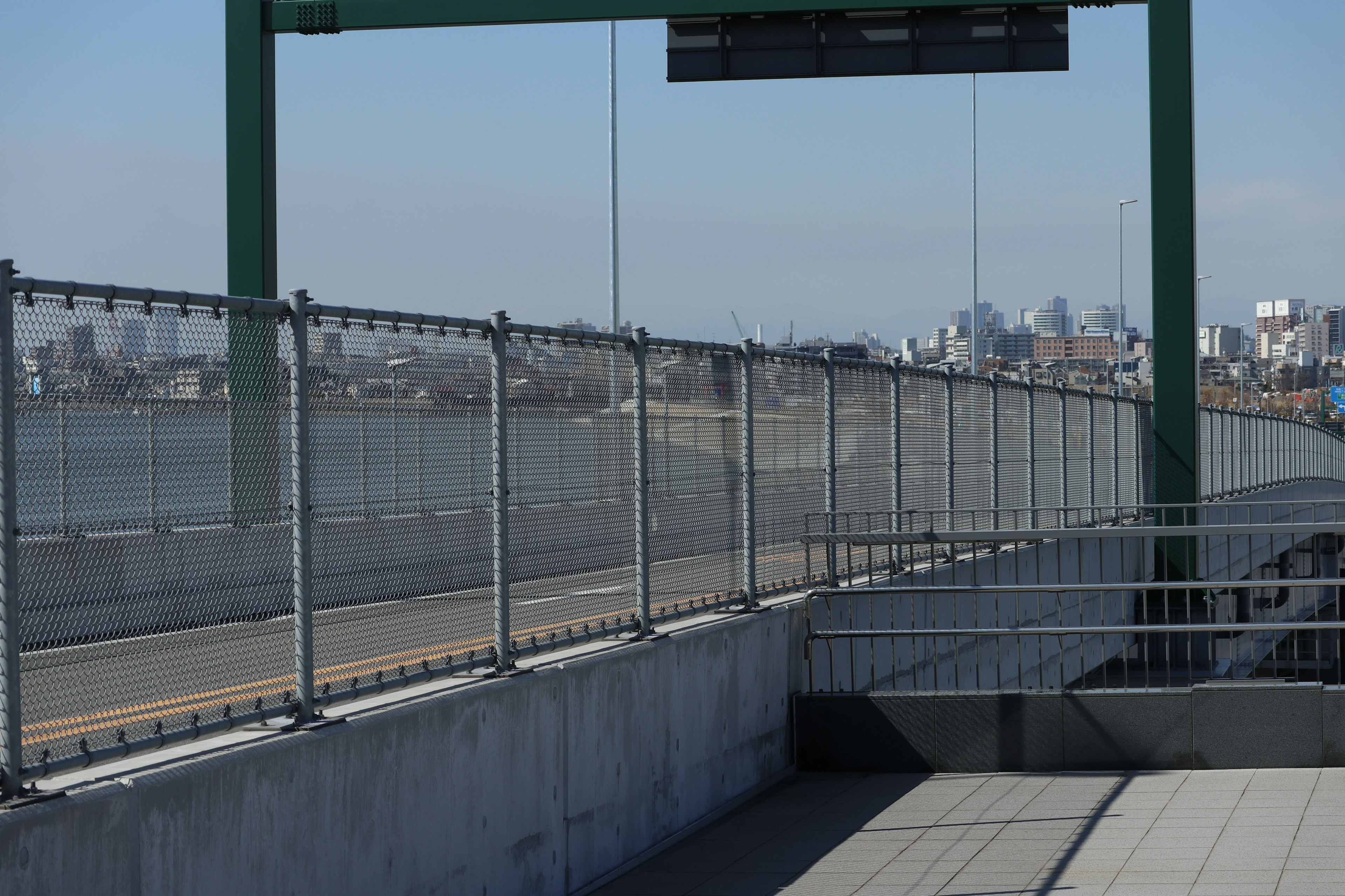 Metal fence along a paved path near a river with a city skyline in the background