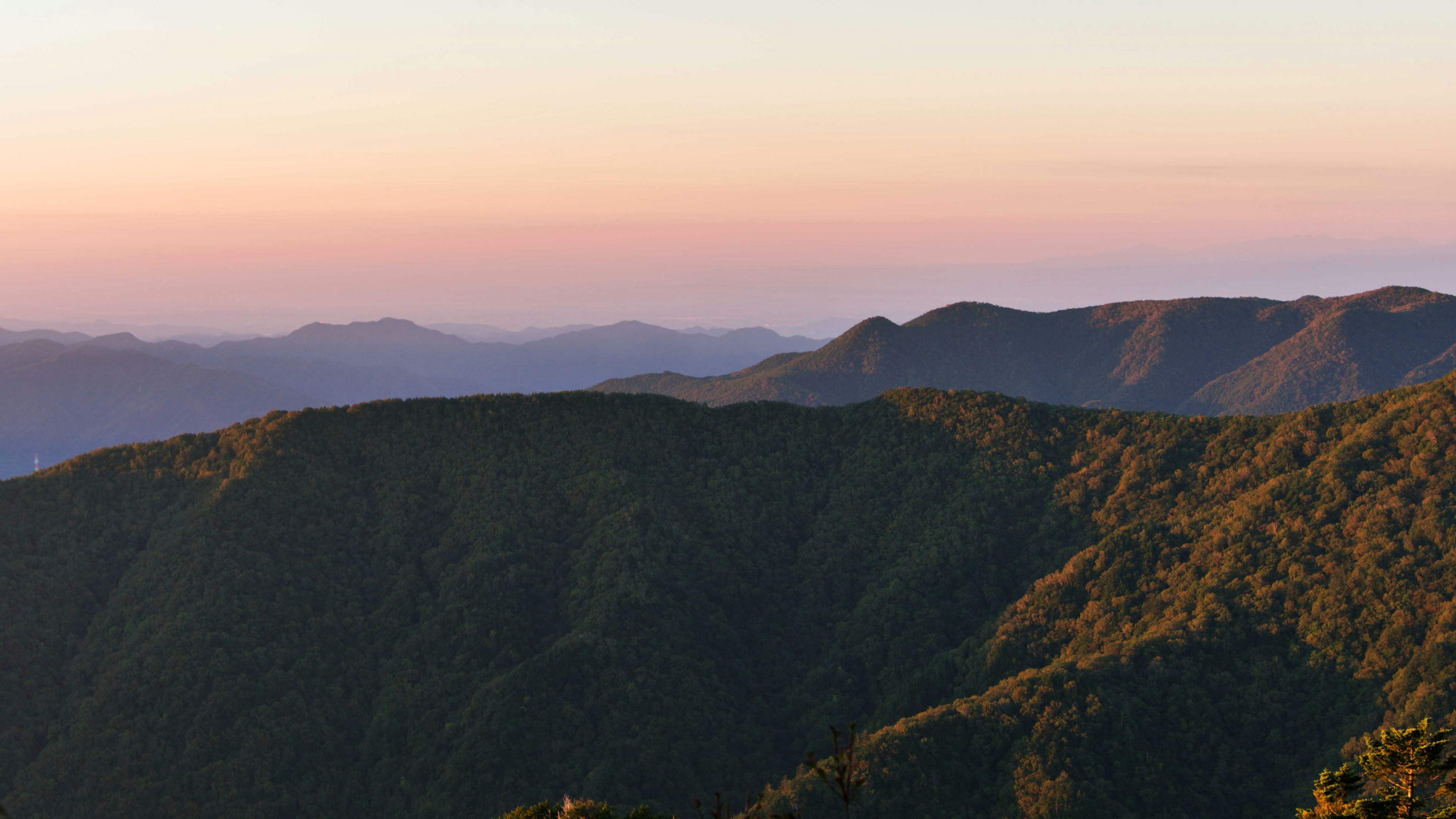 Mountain landscape at sunset featuring green hills and a blue sky