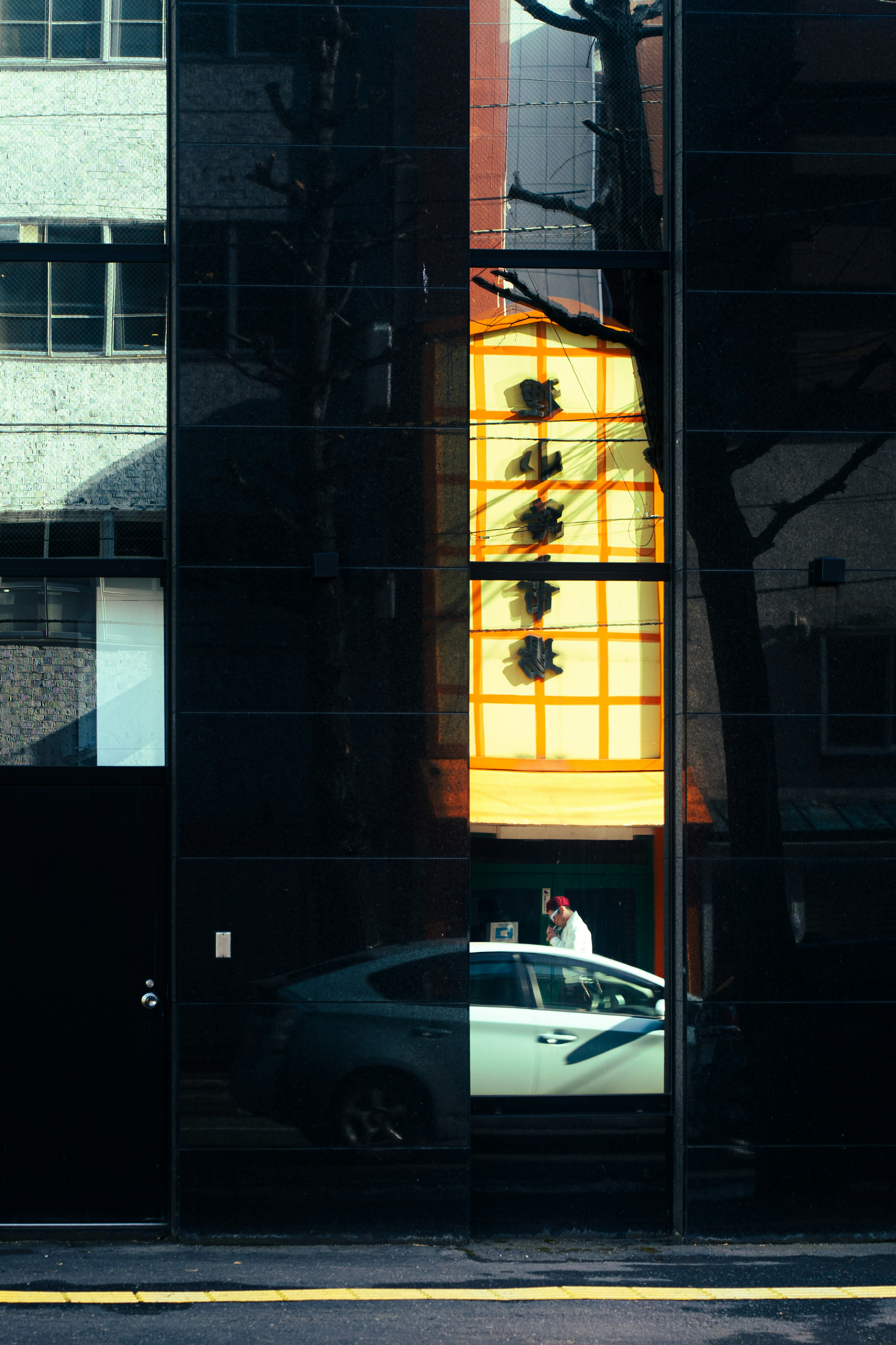 Reflejo de un taxi y una persona en un edificio de vidrio negro con un letrero brillante