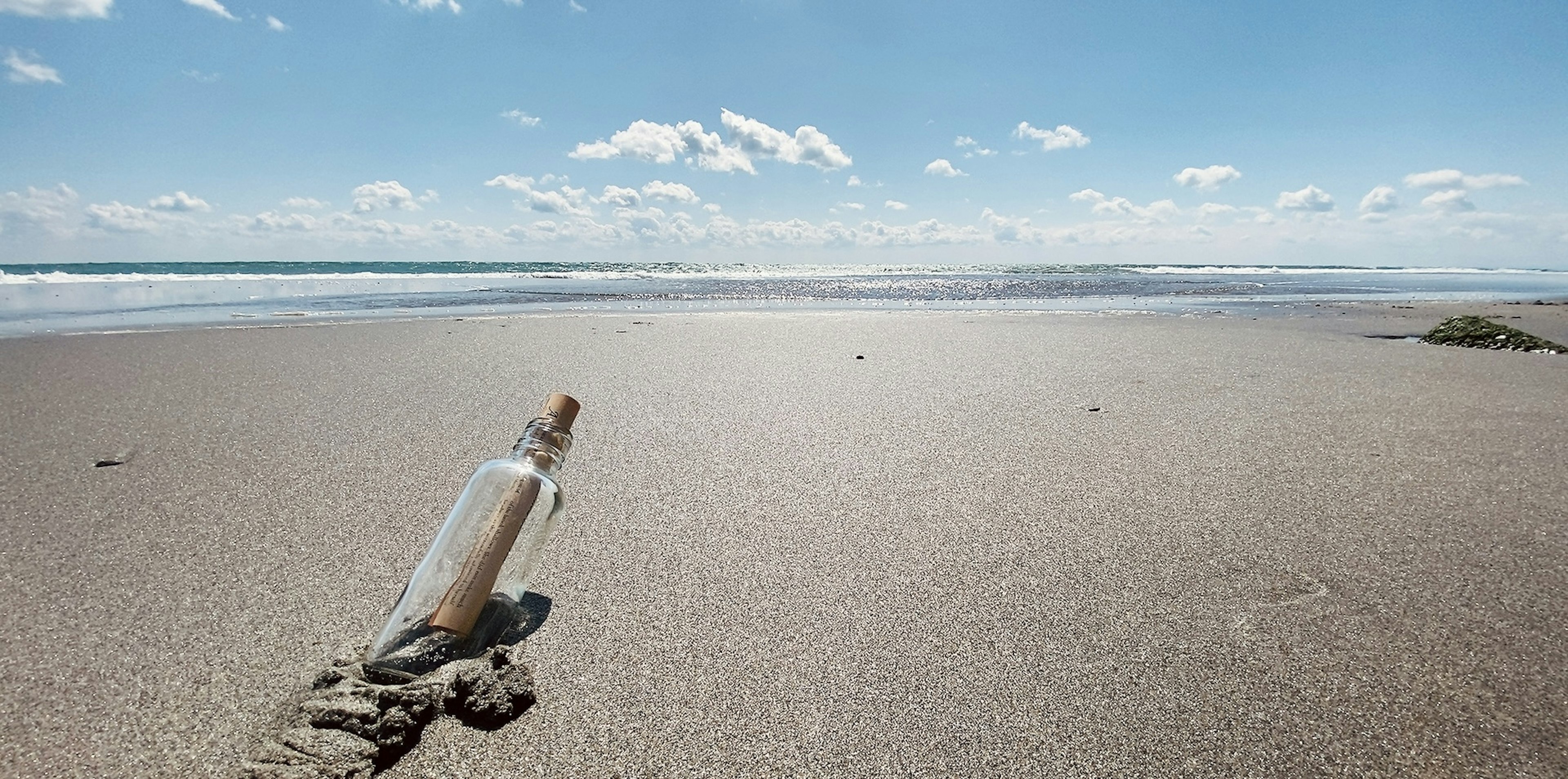 Message bottle on sandy beach with blue sky