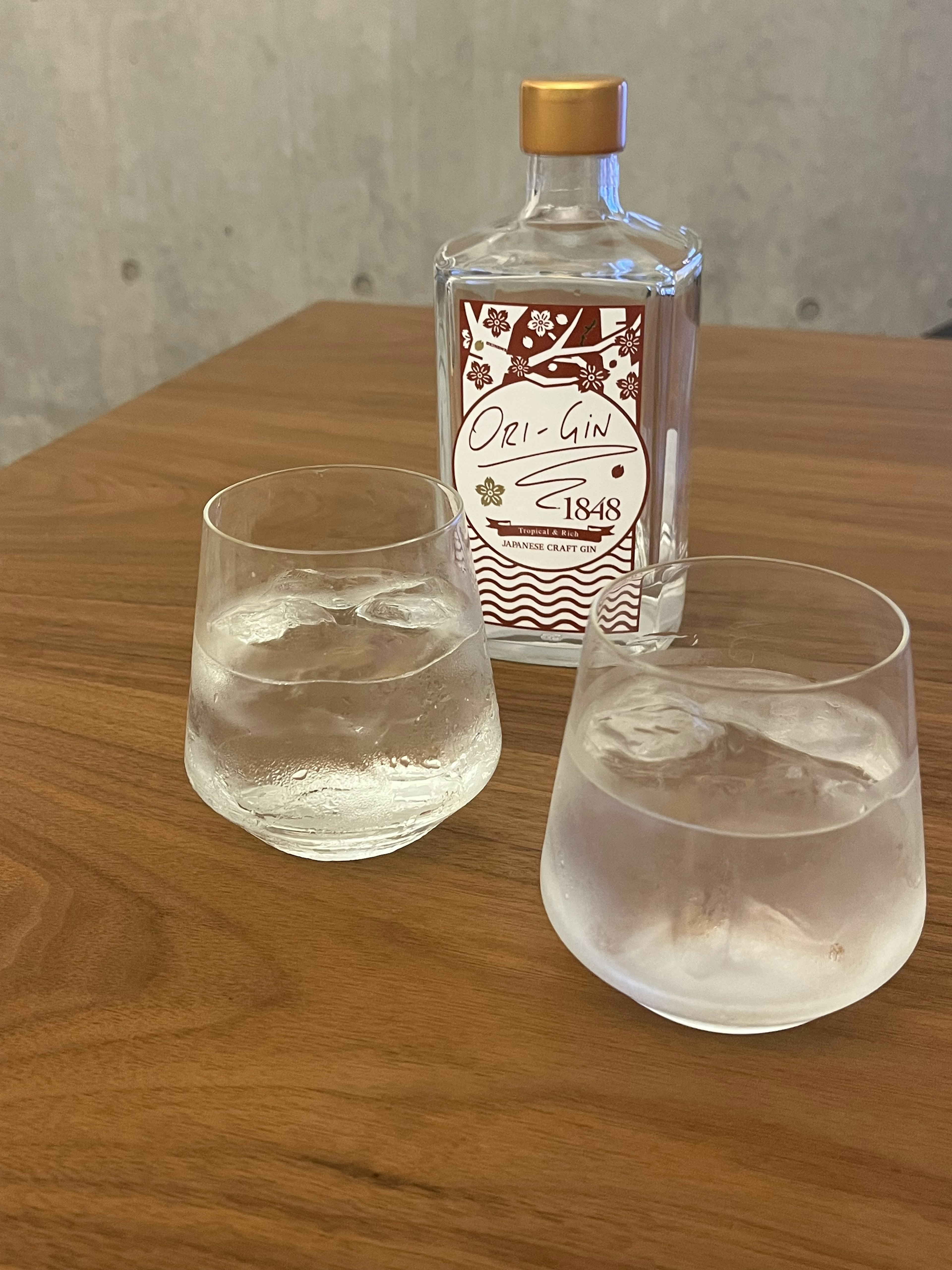 A bottle and two glasses with ice on a wooden table