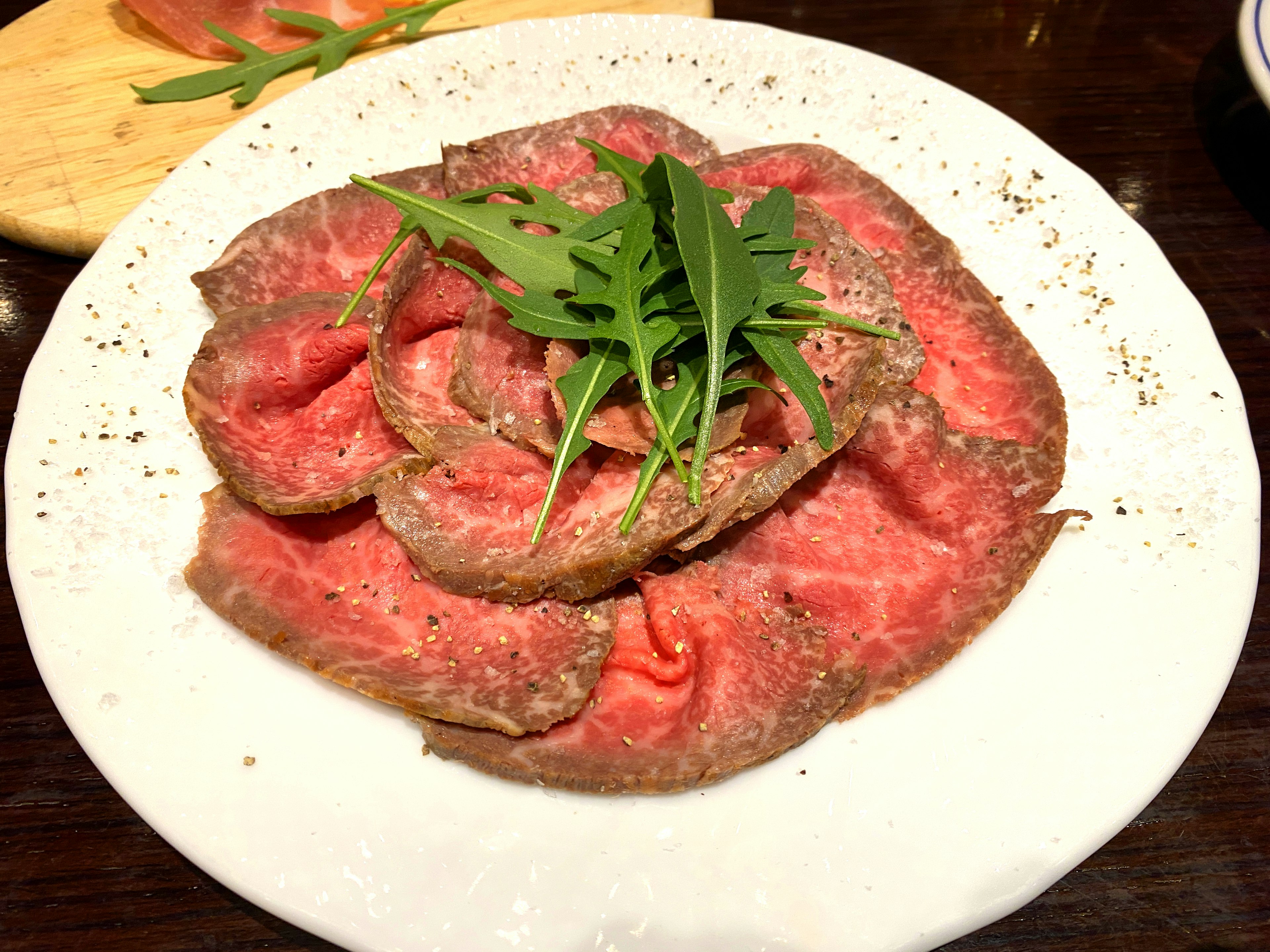 Thinly sliced meat arranged in a circular pattern garnished with fresh herbs