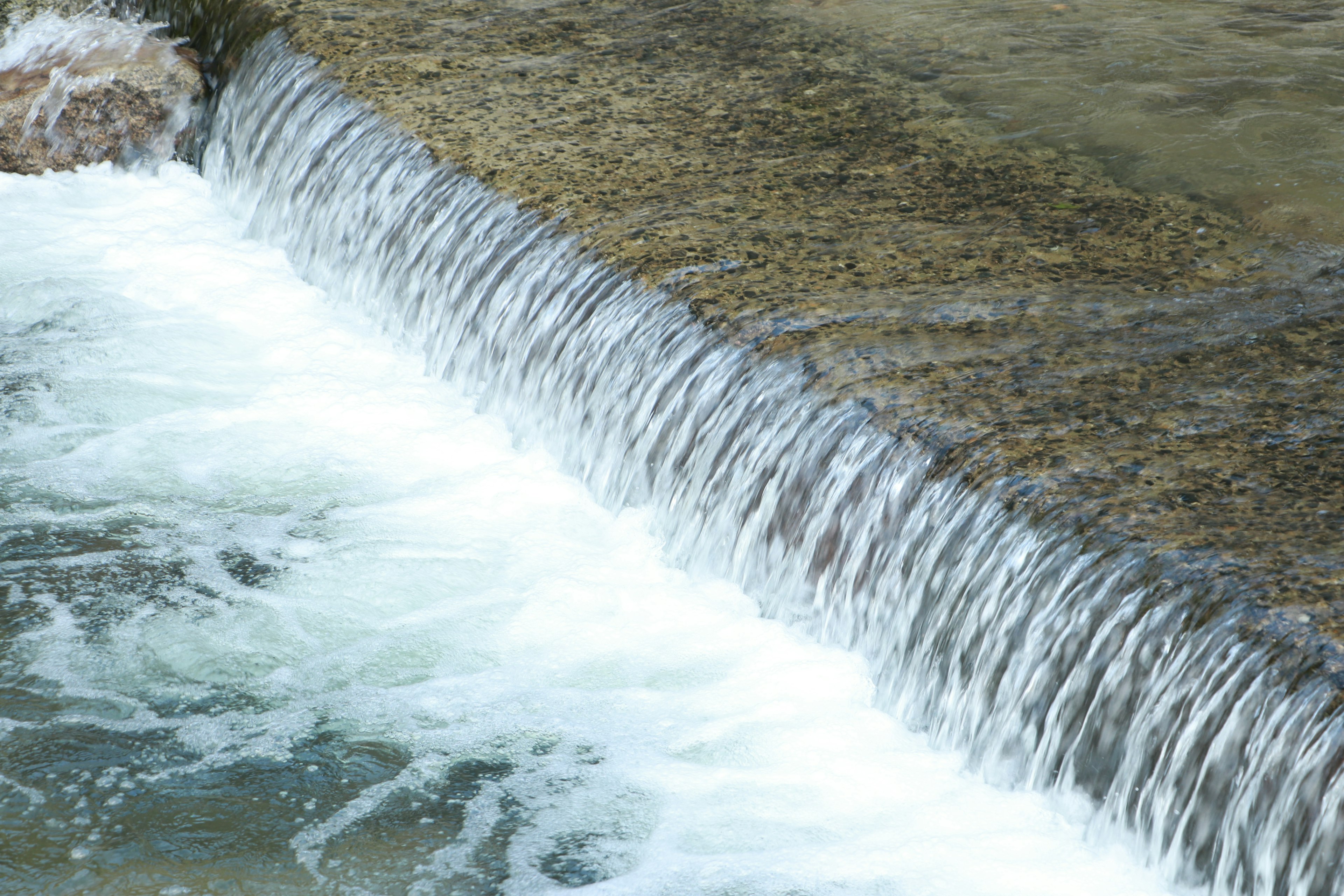 Imagen de un flujo de agua sobre una represa con agua espumosa y parte de una roca visible