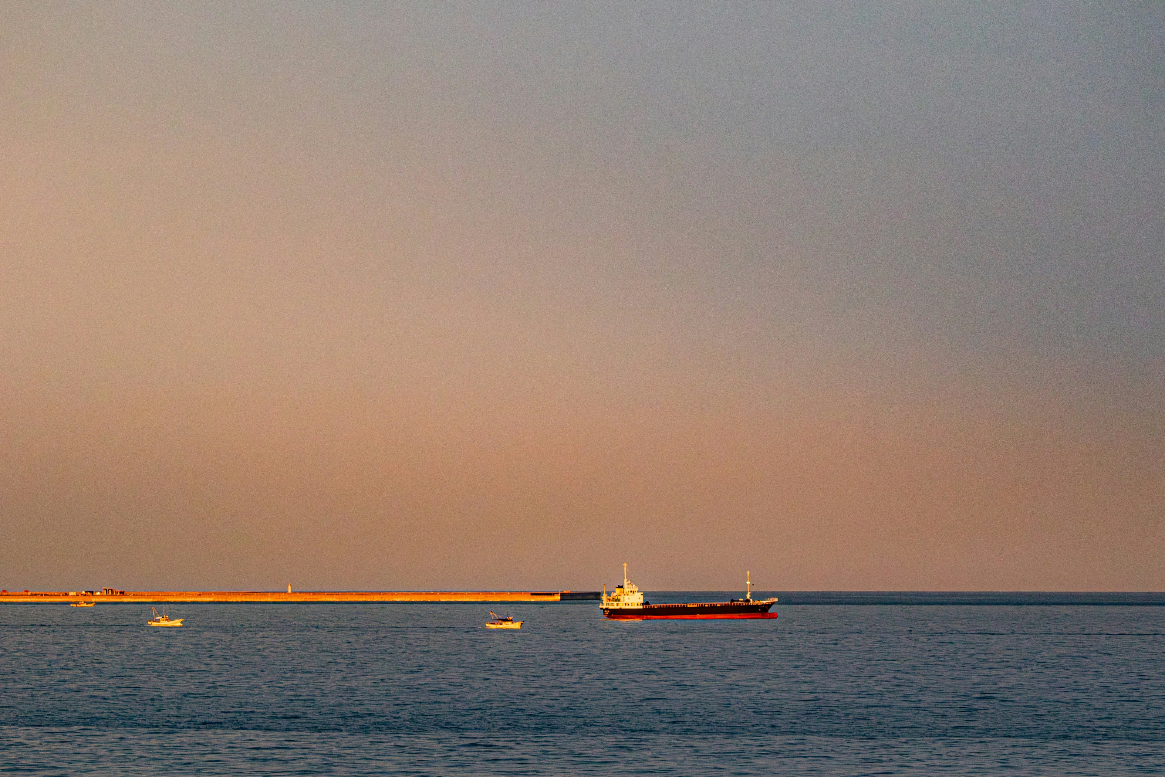 夕暮れの海に浮かぶ船と防波堤の景色