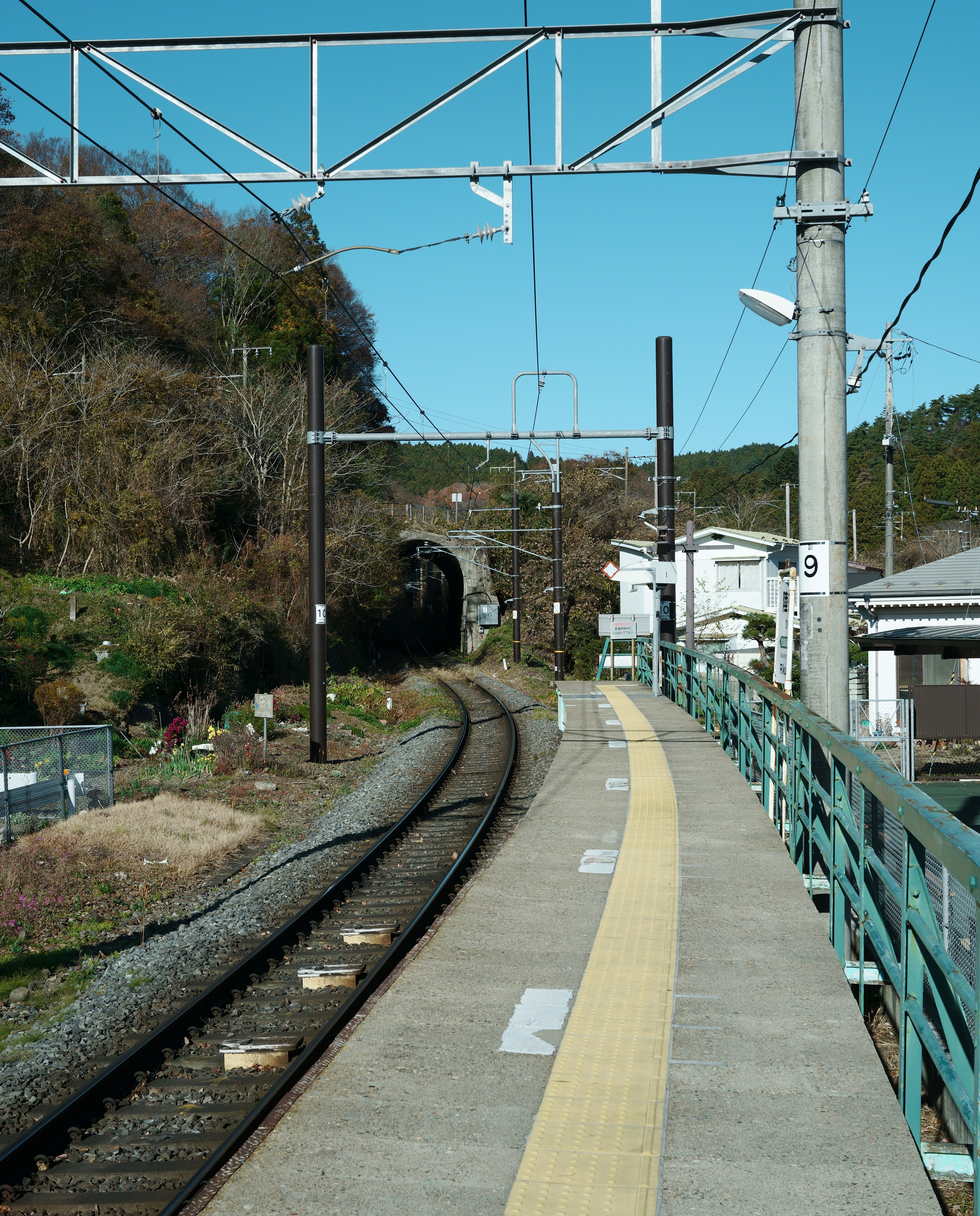 Train station platform with curved tracks under a blue sky