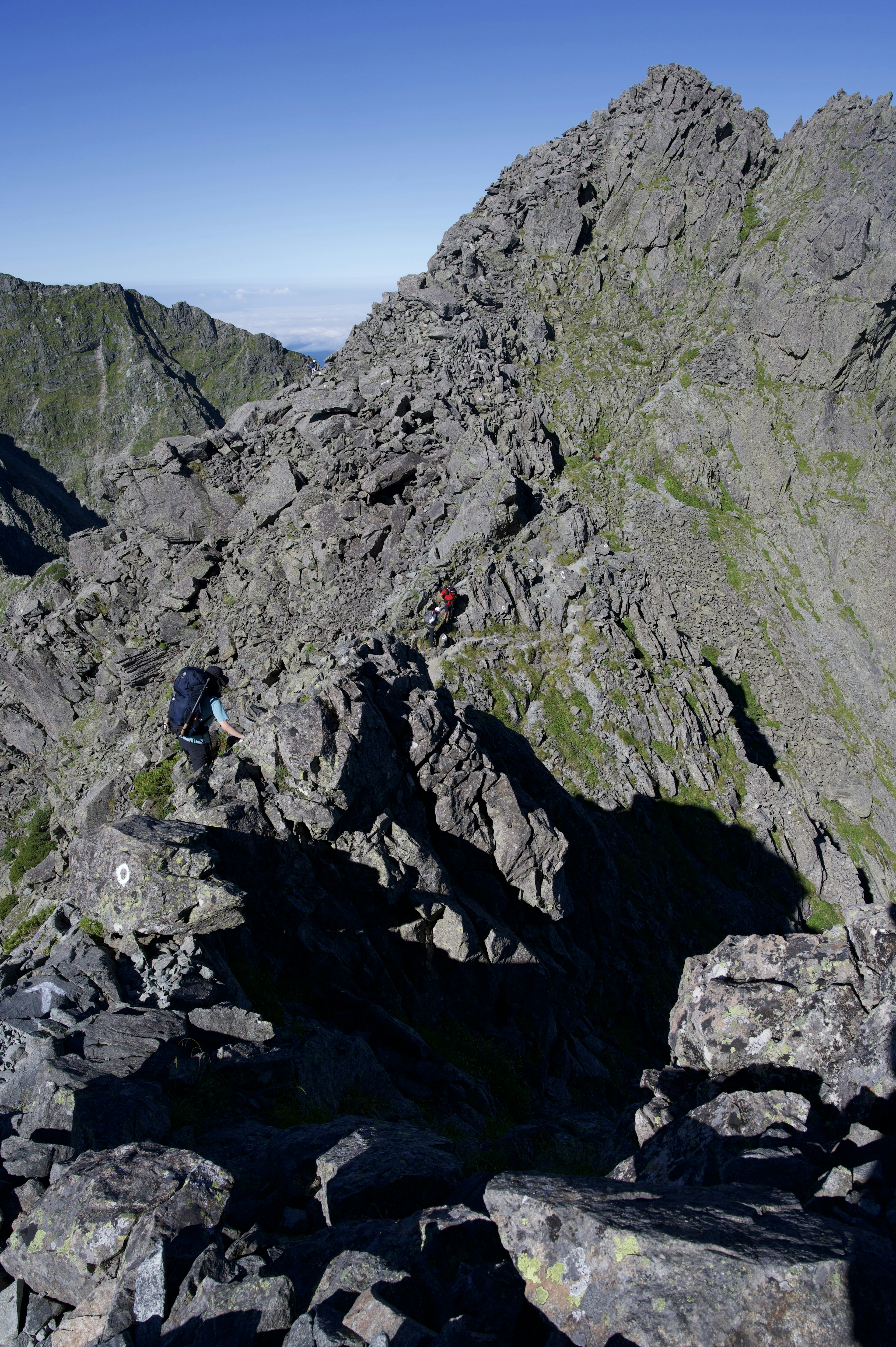 Des grimpeurs naviguant sur un terrain montagneux rocheux sous un ciel bleu clair