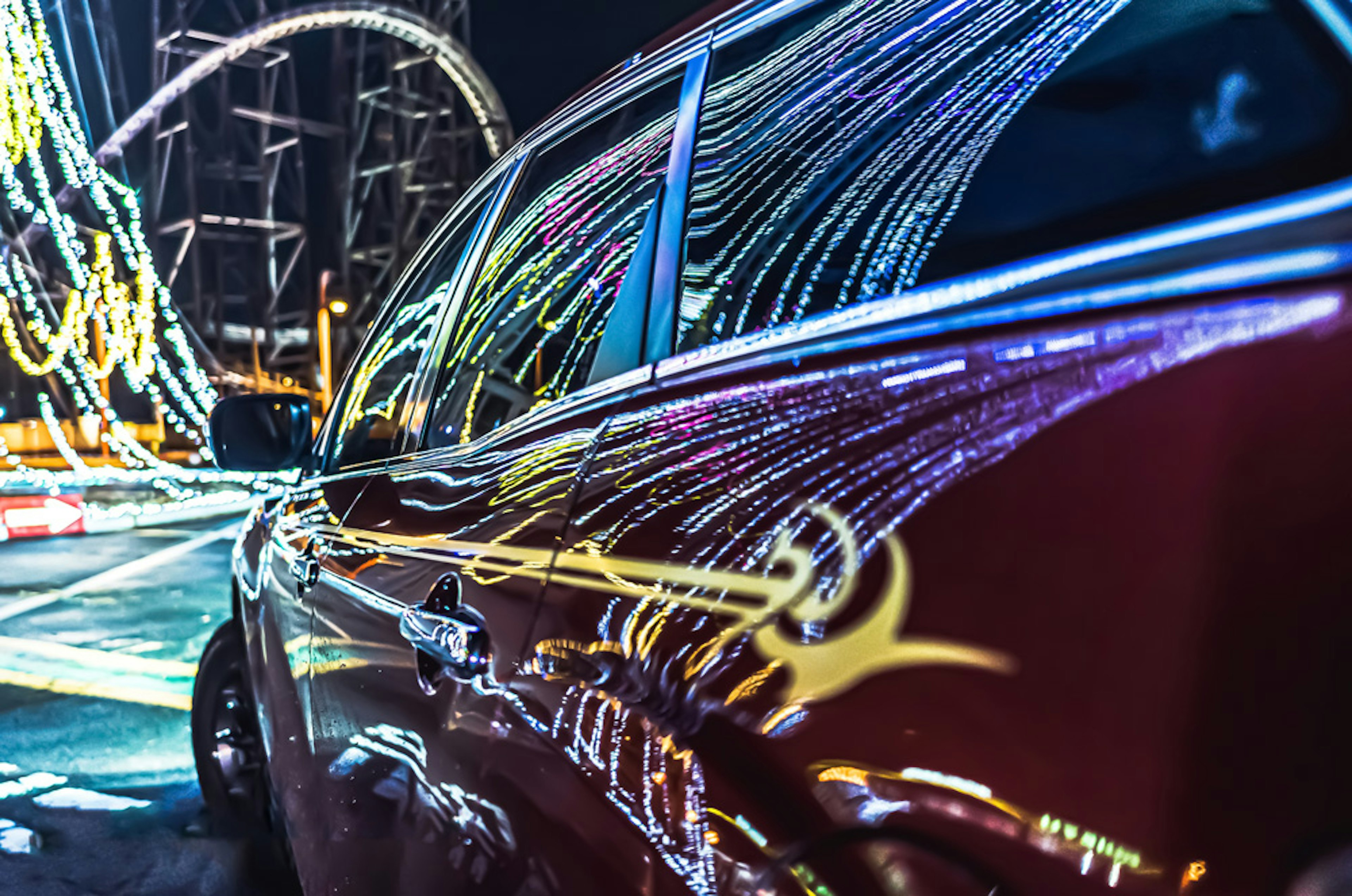 Voiture rouge reflétant des traînées lumineuses colorées la nuit