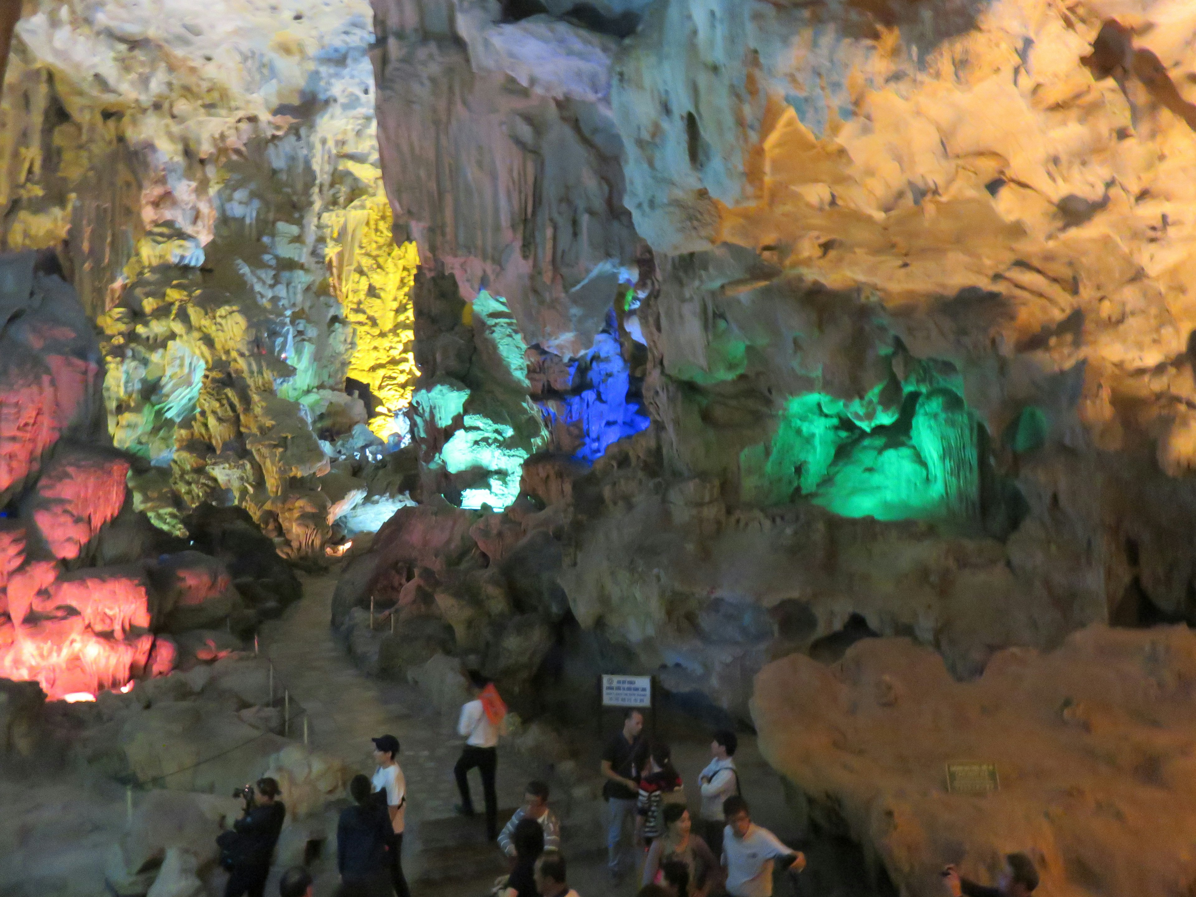 Interior of a cave illuminated by colorful lights with tourists walking