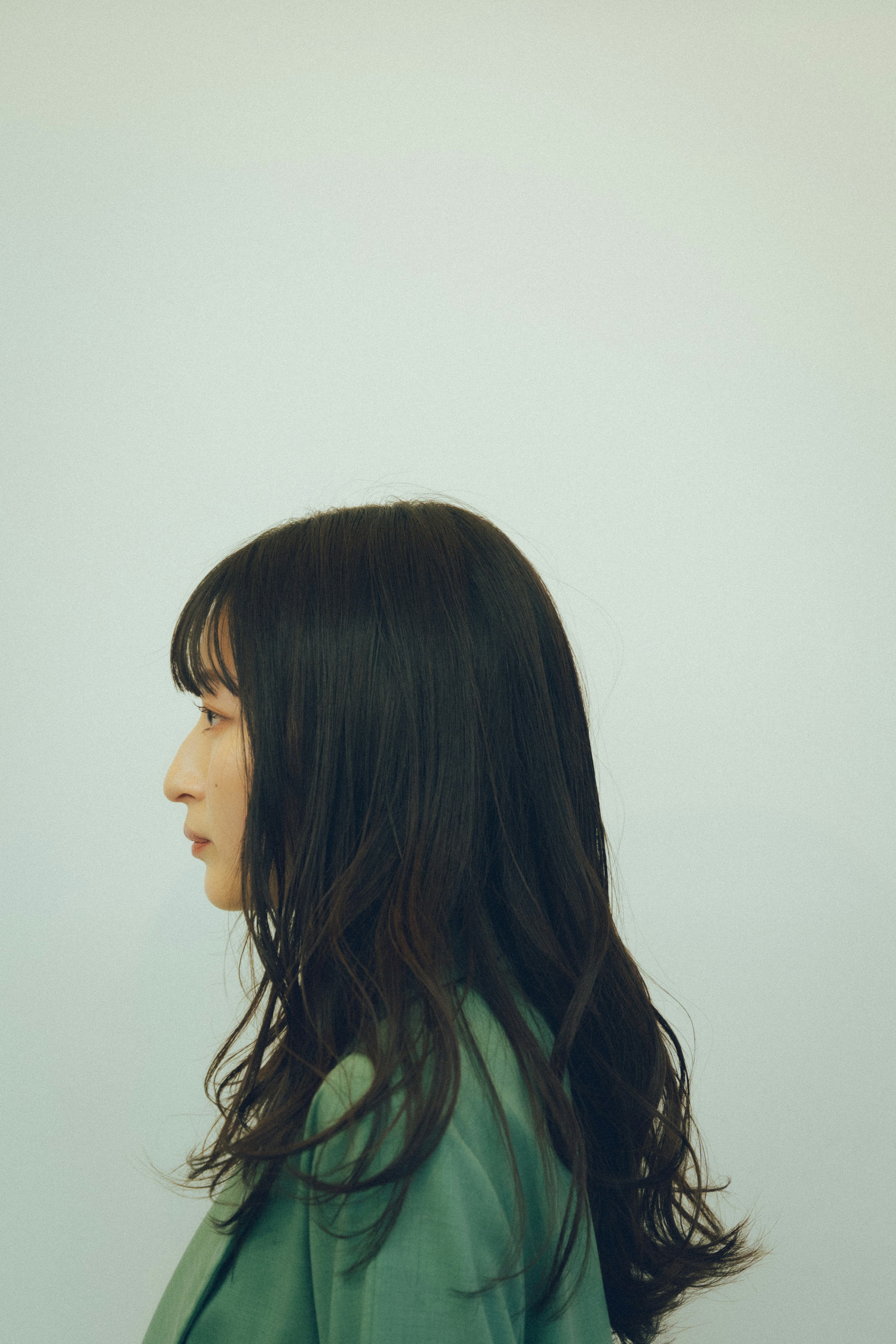 Profile view of a woman with long wavy hair wearing a green jacket