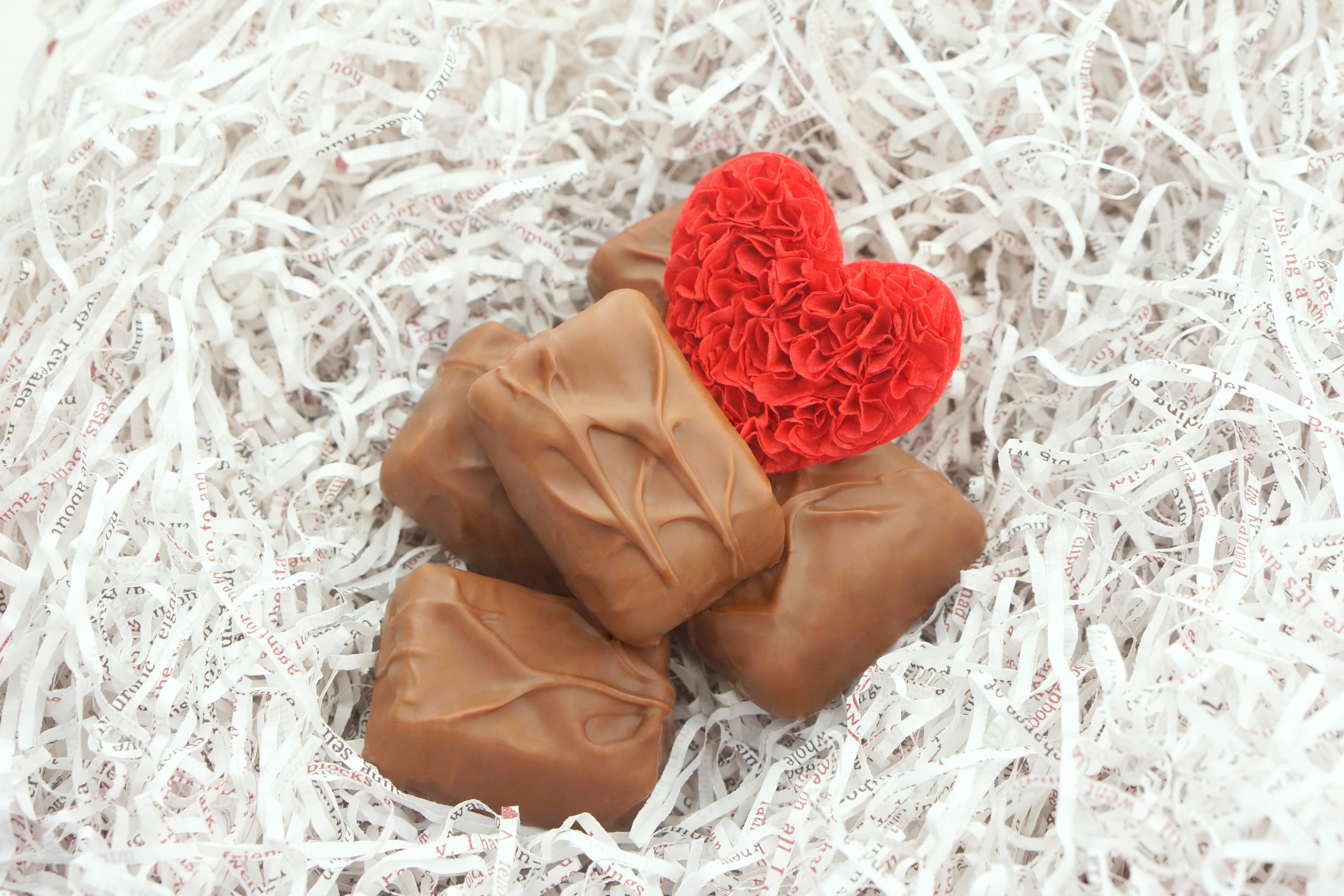 Un objet en forme de cœur rouge et des morceaux de chocolat placés sur du papier déchiqueté blanc