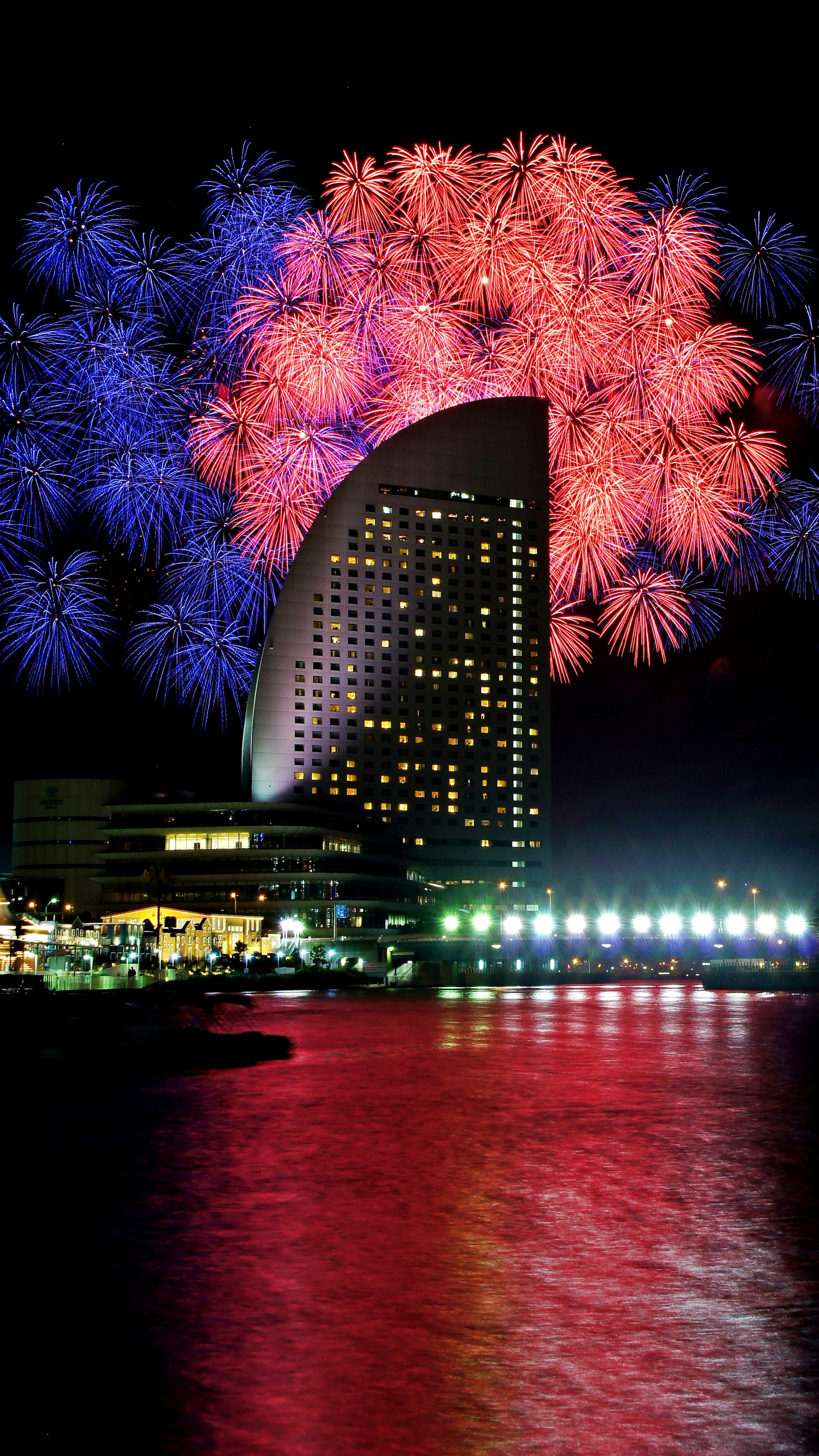 Nighttime scene featuring fireworks over a modern building by the water