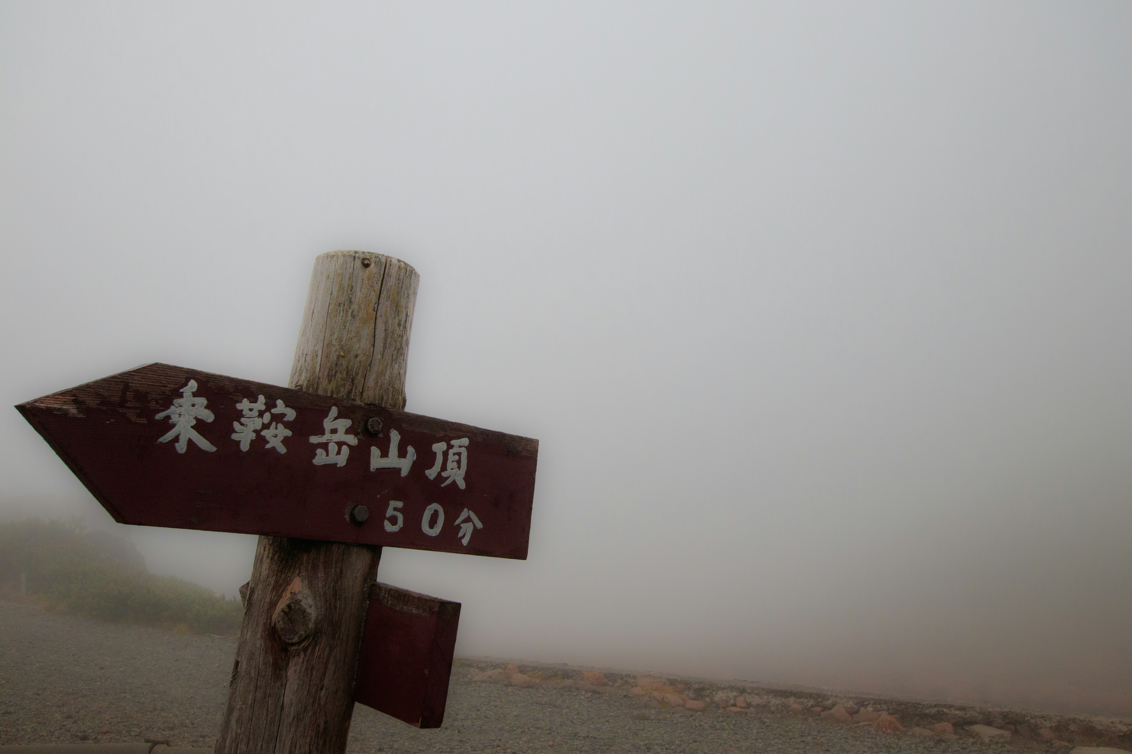 Señal de madera en la niebla que indica la distancia hasta la cima de la montaña