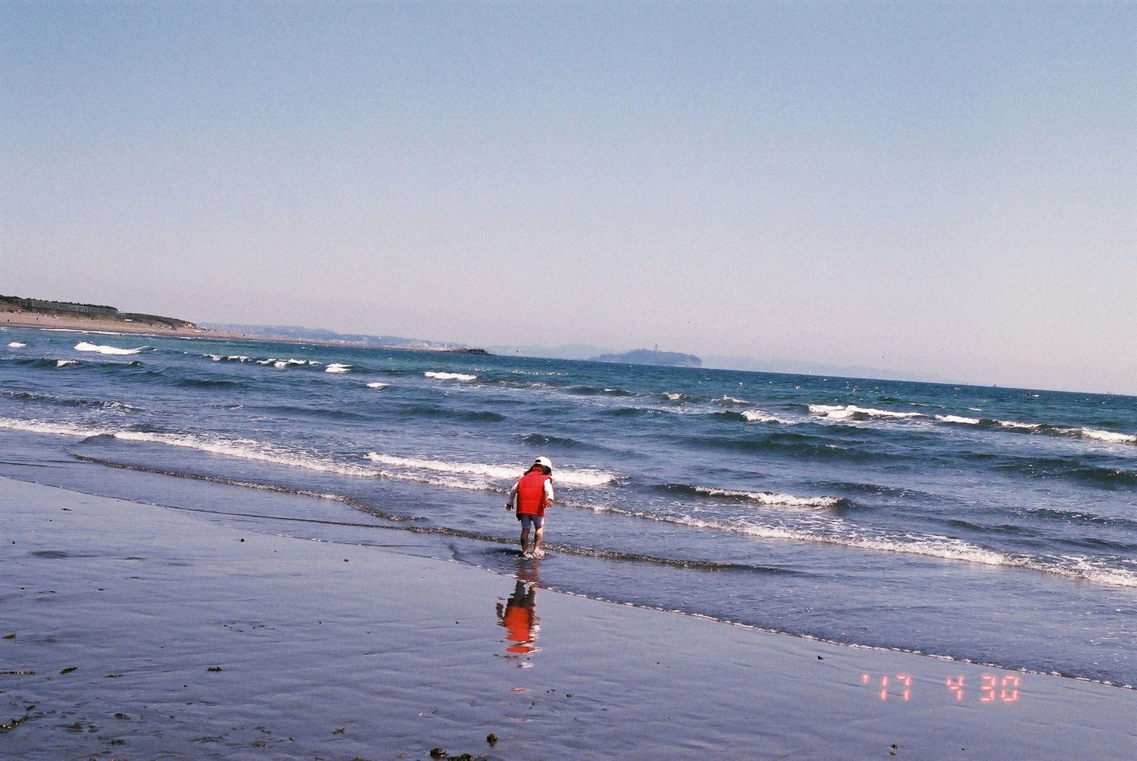 เด็กในเสื้อผ้าสีแดงเดินอยู่ริมชายหาด