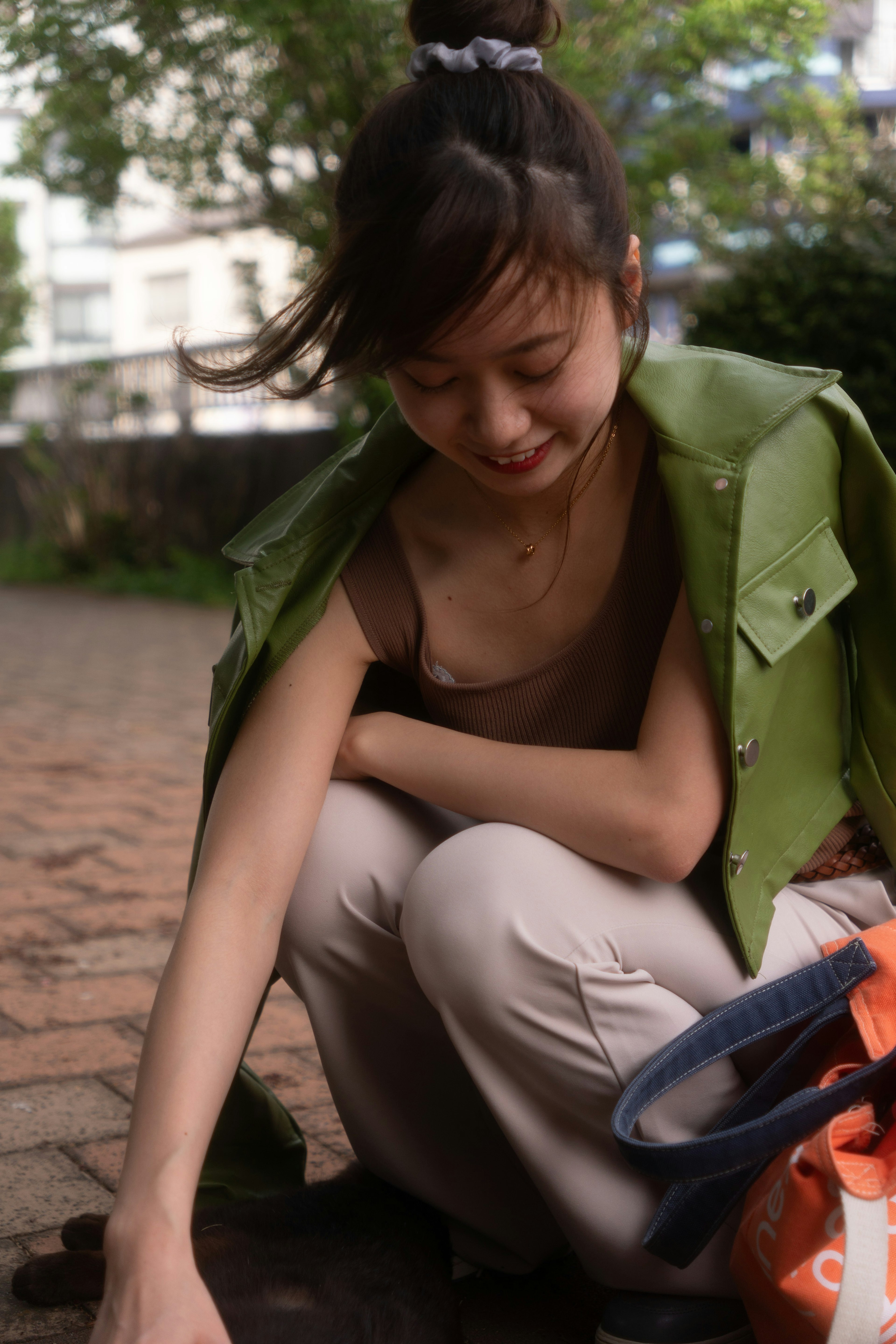 A woman in a green jacket crouching down looking at something on the ground