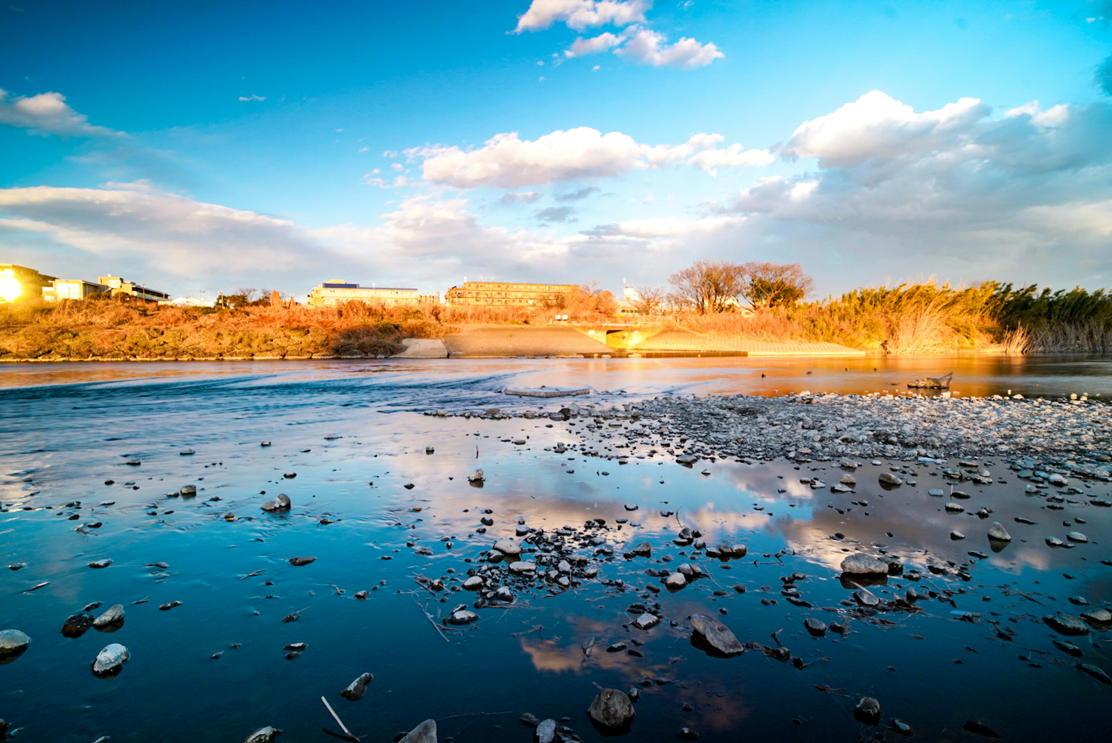 Tranquil water surface reflecting blue sky and clouds with scattered stones