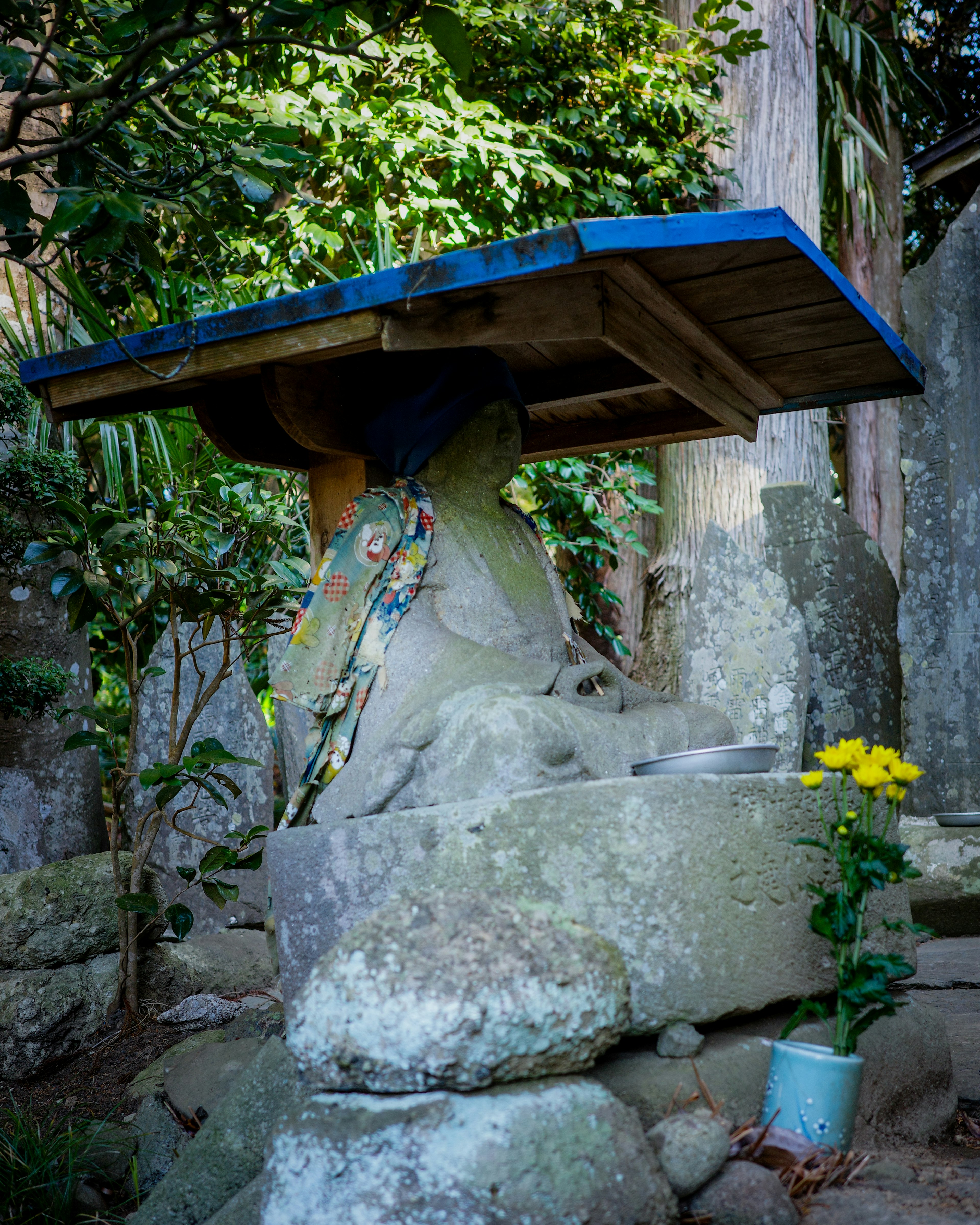 石造の水場に青い屋根と黄色い花がある風景